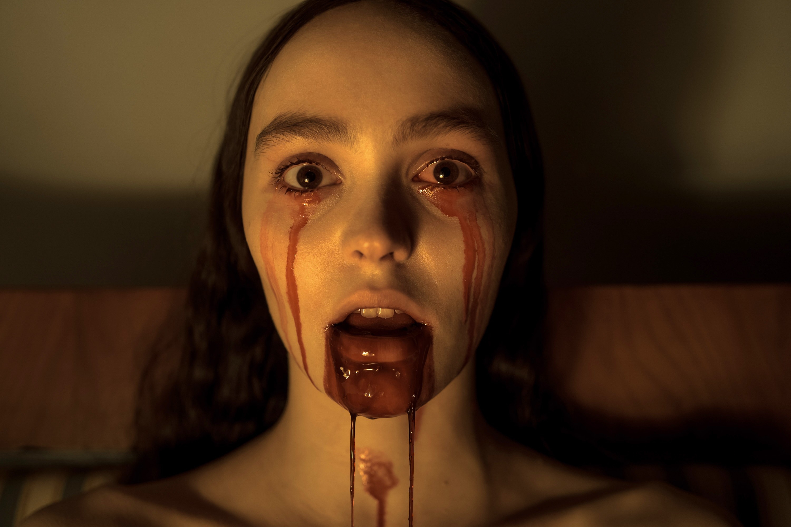 Person with long hair looks shocked with fake blood streaming from eyes and mouth, resembling a horror scene