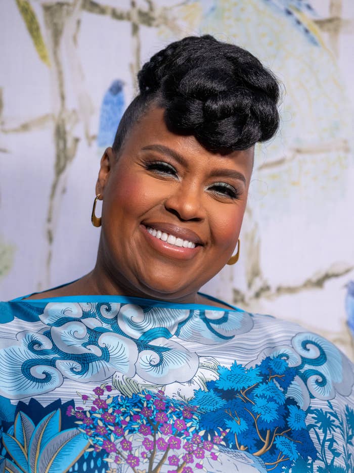 Person smiling, wearing a patterned outfit with nature motifs. Their hair is elegantly styled, and they appear at a celebrity event