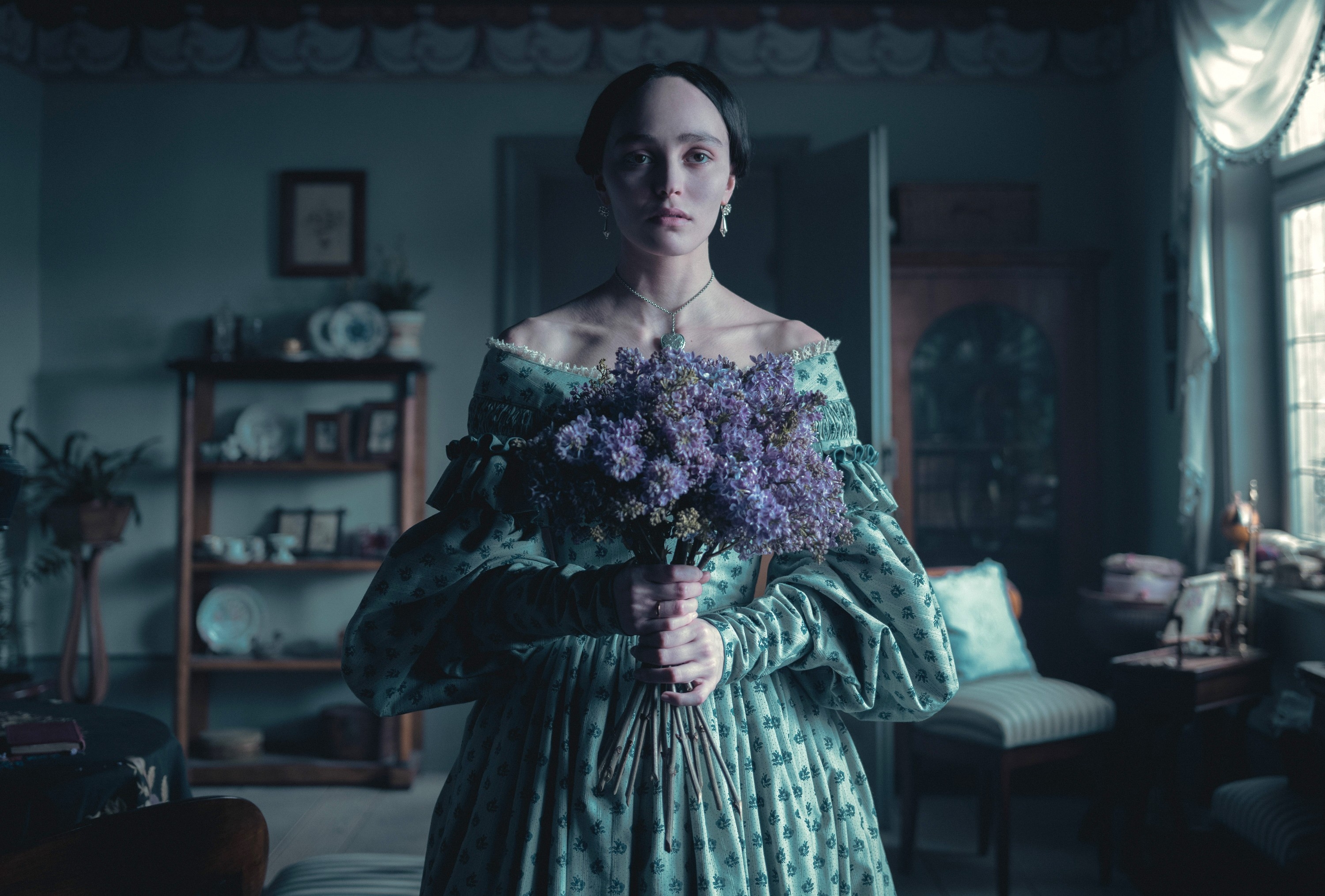 Person in period-style dress holding a bouquet of flowers, standing in a vintage room