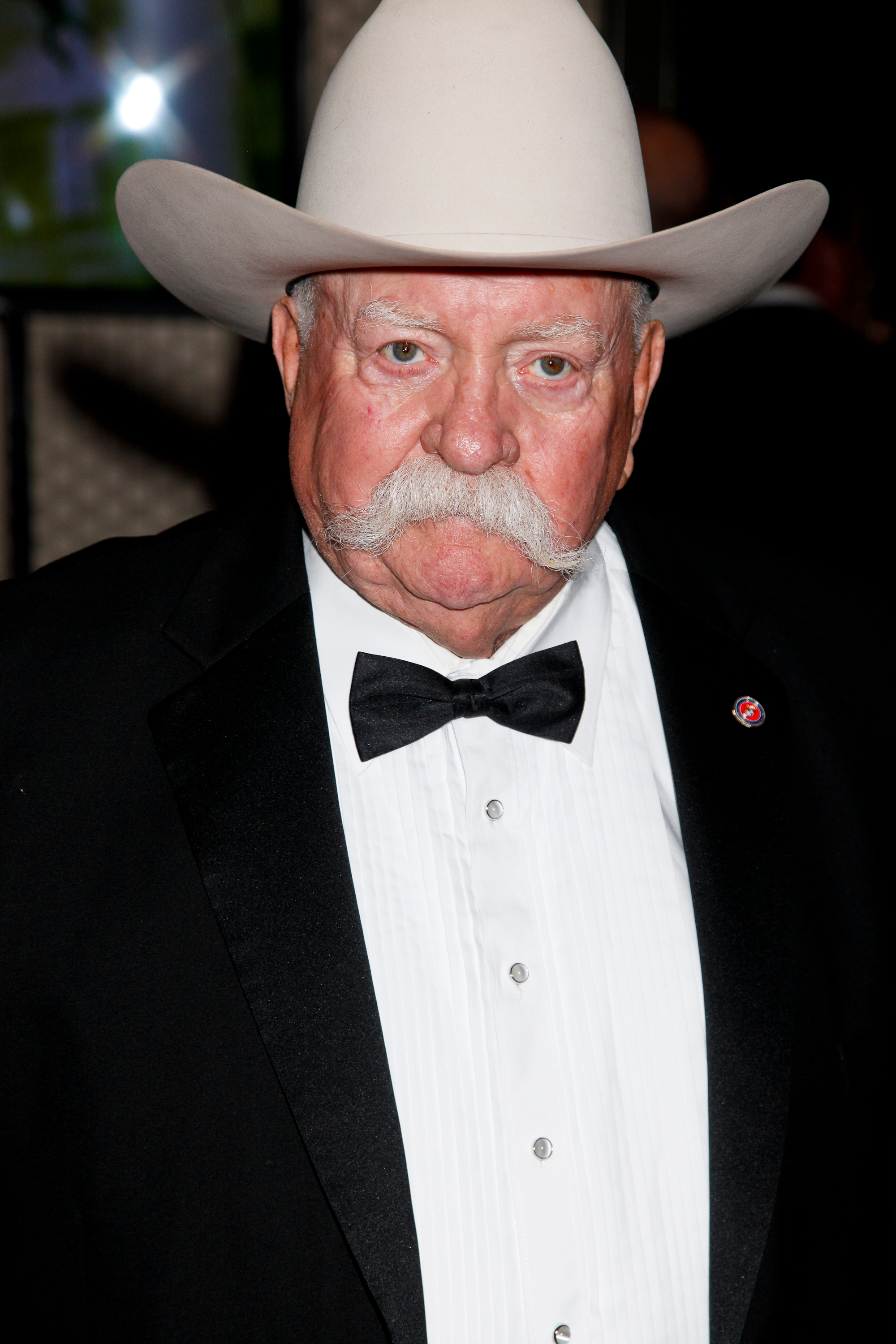 A man in a tuxedo and cowboy hat with a large mustache poses for a photo, exuding a classic and distinguished style