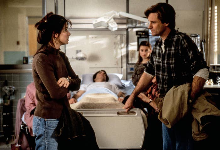 Scene from a hospital room with two people talking beside a patient's bed. The setting suggests an emotional or pivotal moment in a movie