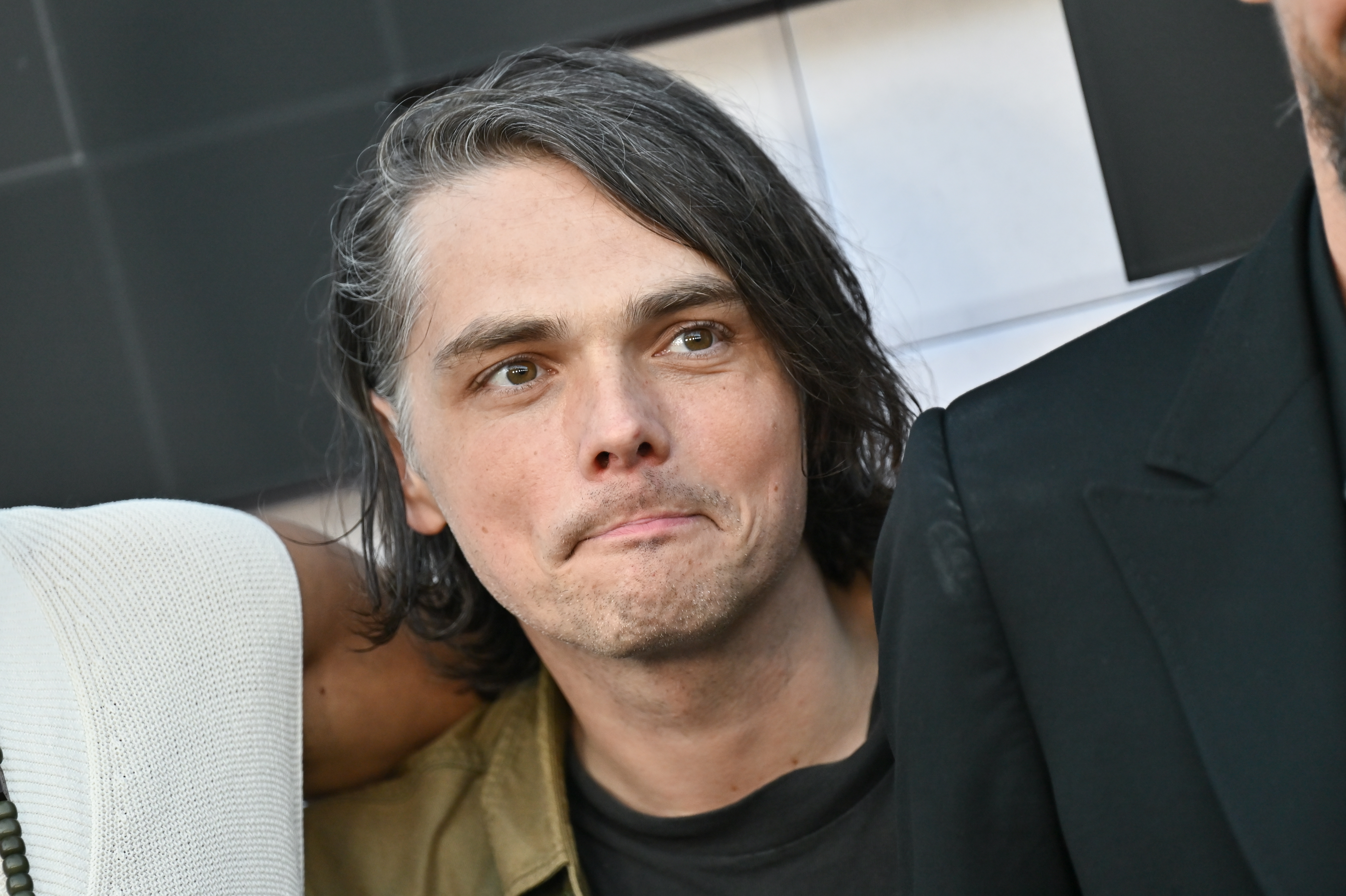 A person with medium-length hair looks upward, wearing a casual jacket, surrounded by others in close proximity