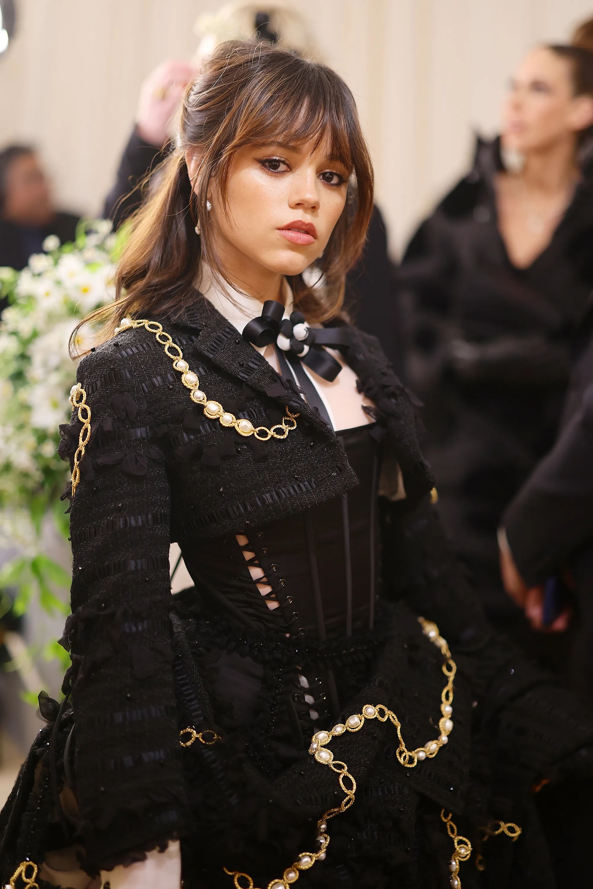 Person in an ornate black dress with gold chain details and a black and white bow, posing at an event