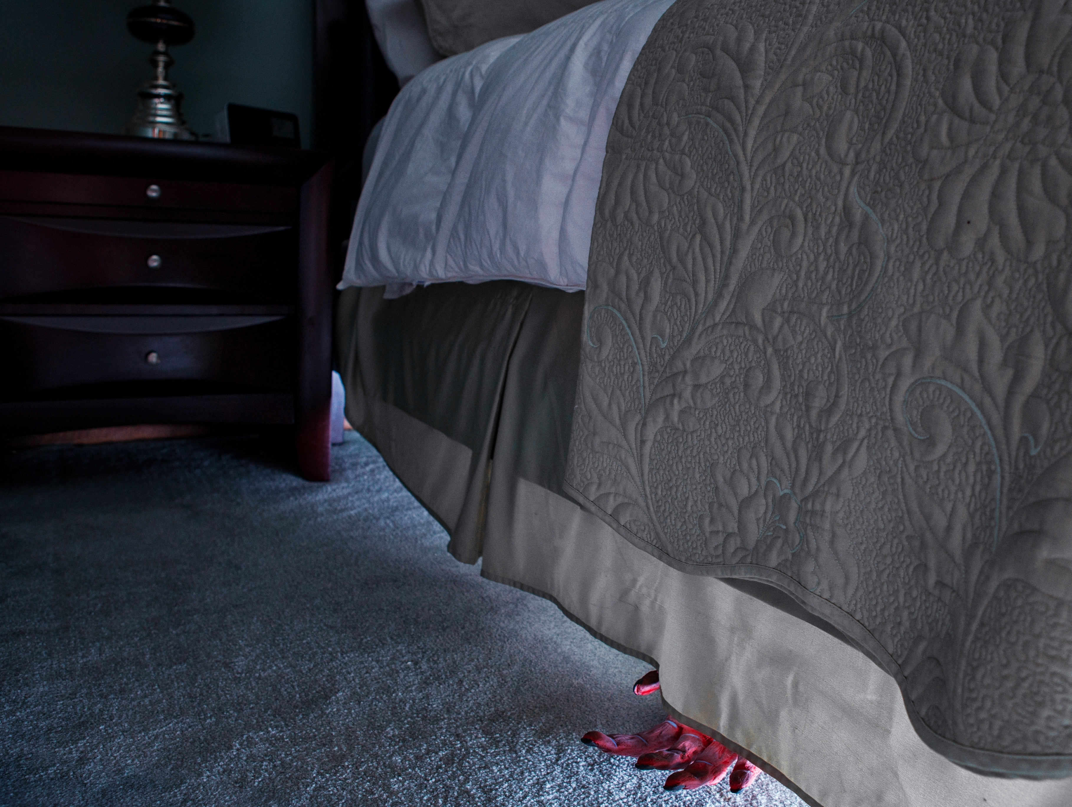 A toy crab peeks out from under a bed with an intricately patterned bedspread, near a dark wooden nightstand