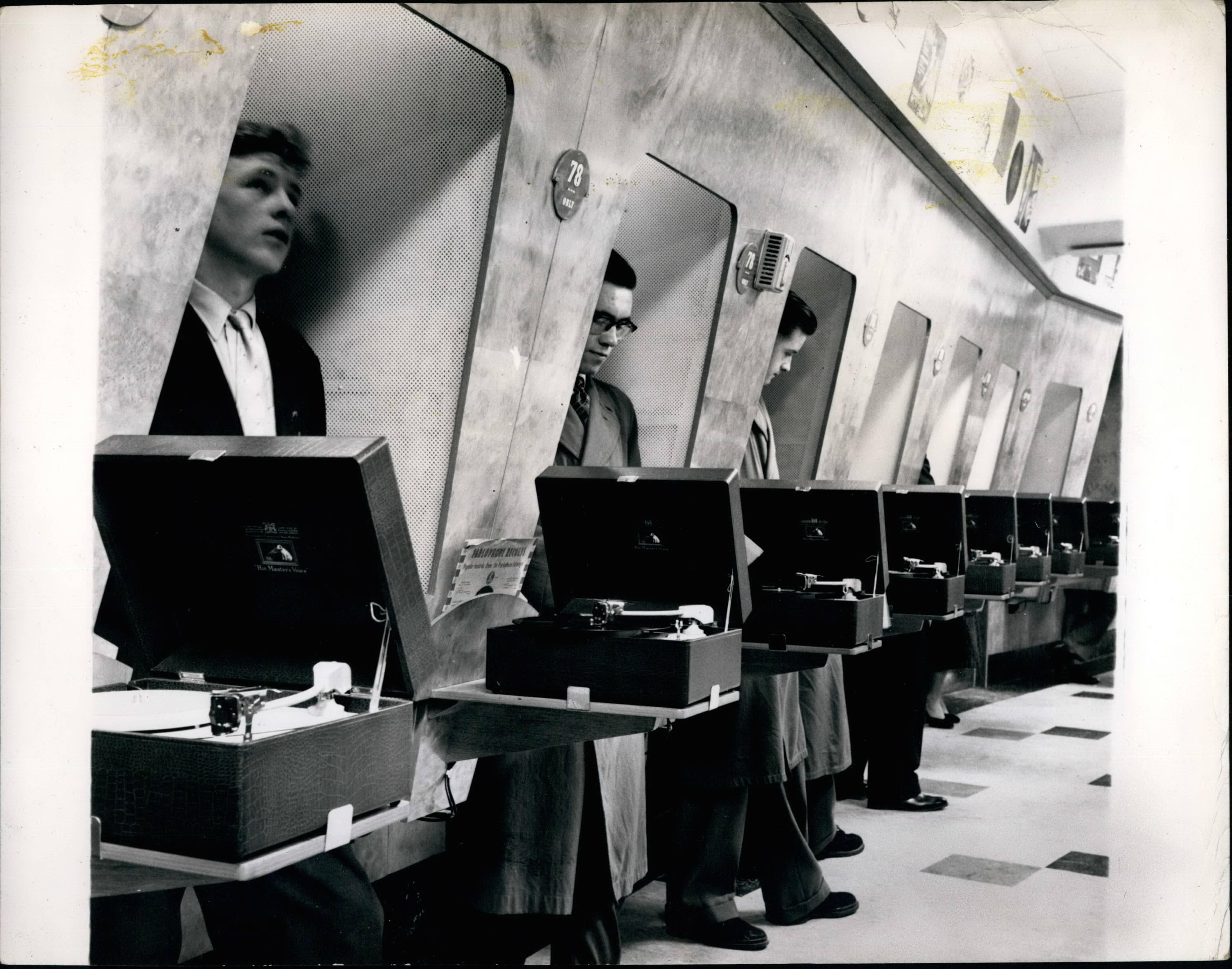People stand in soundproof listening booths with turntables to preview records in a vintage music shop