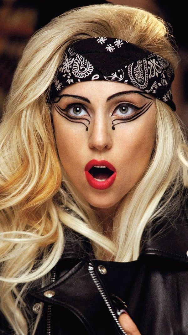 Persona con maquillaje llamativo y pañuelo con diseño paisley, mira sorprendida. Lleva chaqueta de cuero. Estilo dramático y artístico