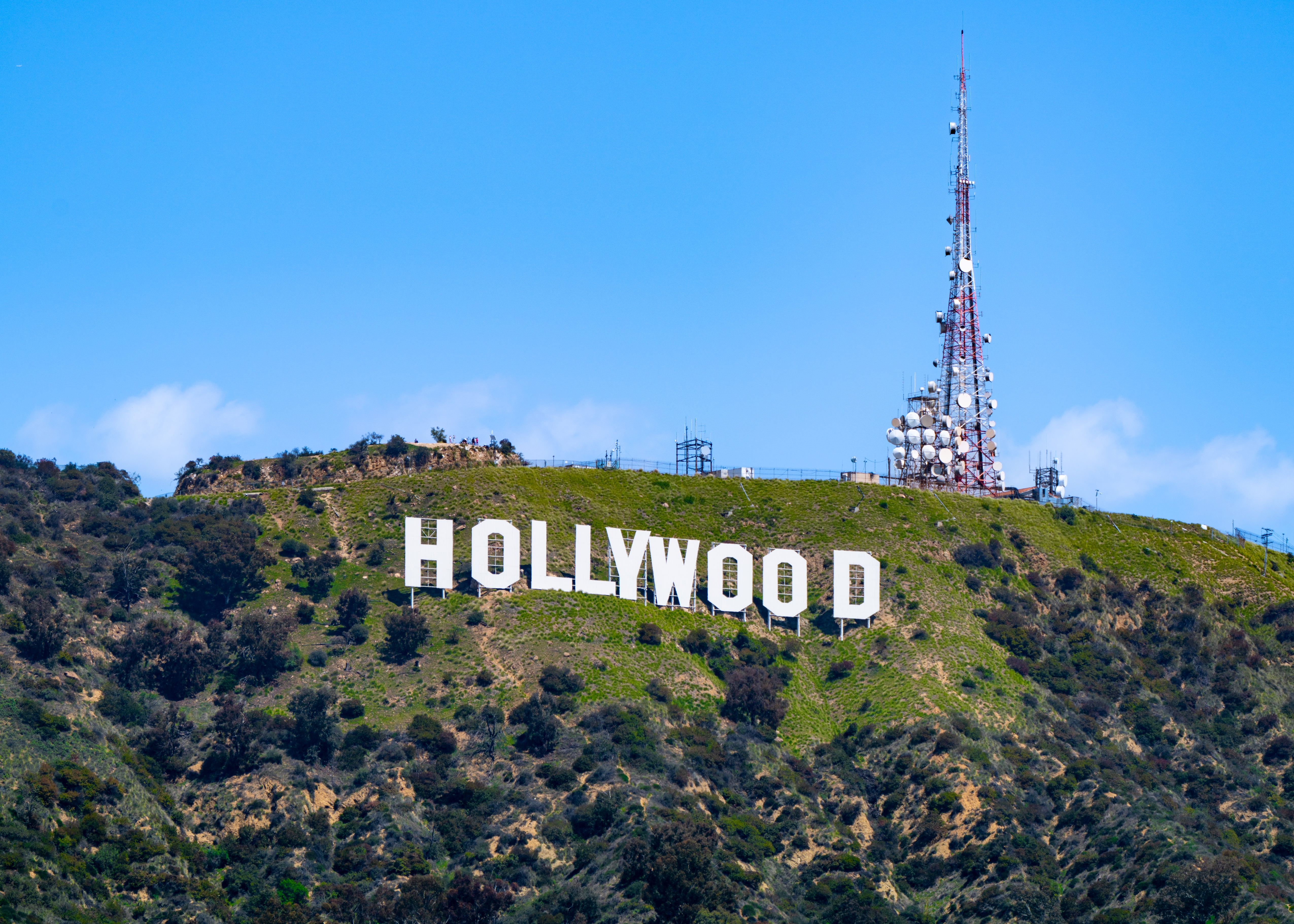 Hollywood sign on a hillside with radio tower above, under a clear sky