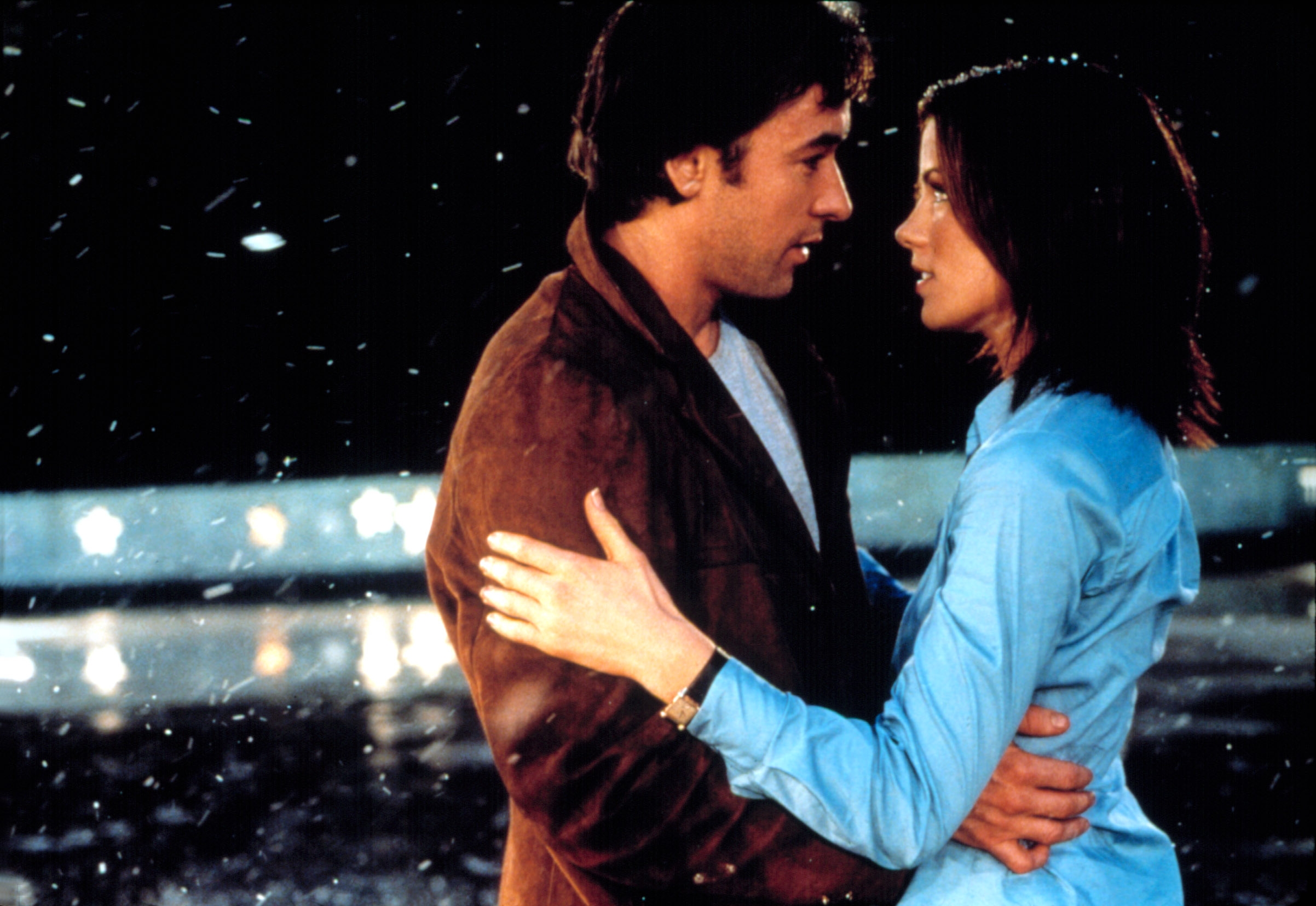 Two people standing close, gazing at each other tenderly, with snow falling around them, creating an intimate moment