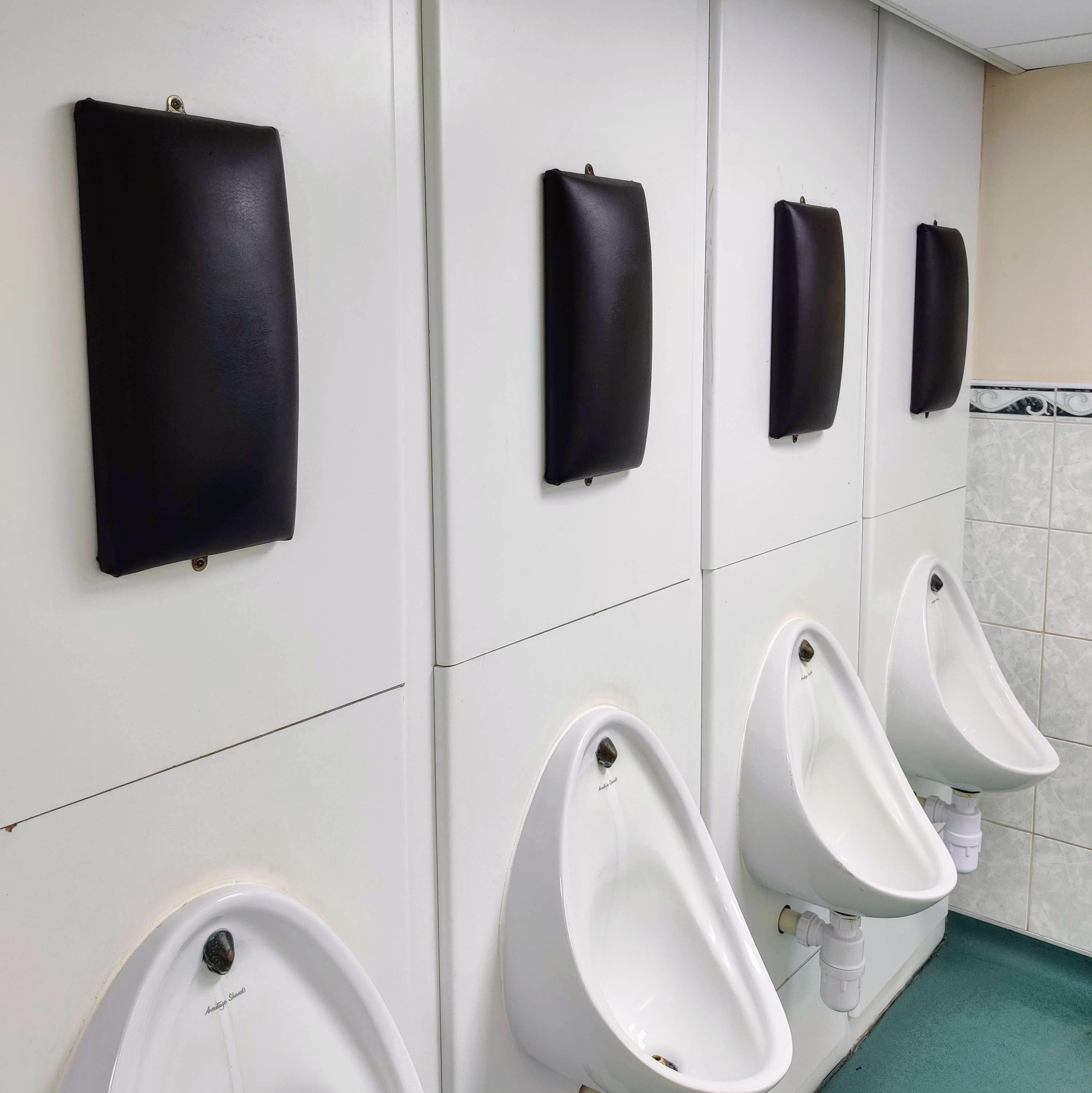 Urinals in a row, partitioned by white panels, with black padding on walls above each urinal