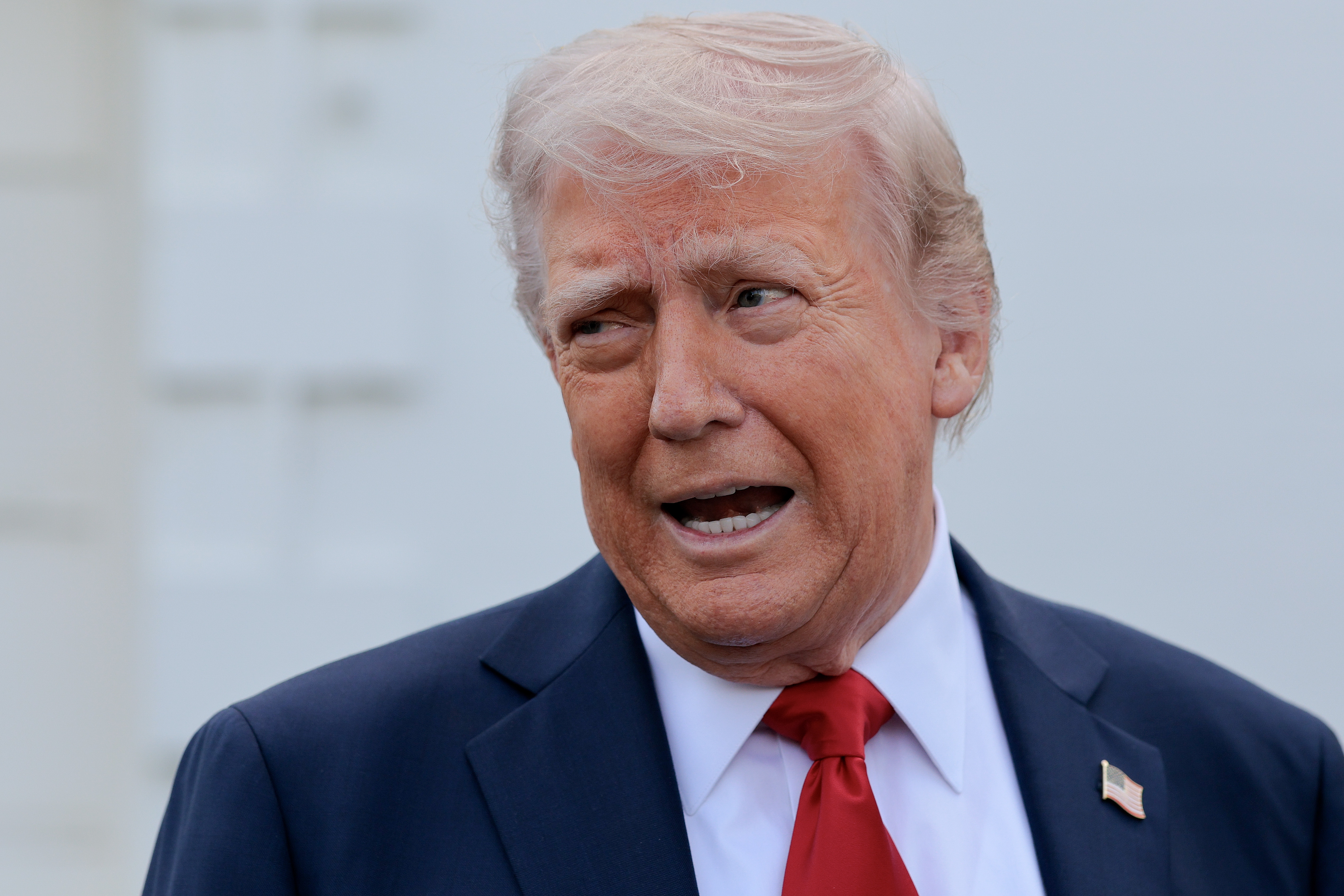 A man in a suit with a red tie is speaking animatedly outdoors