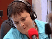 Person smiling and speaking into a red microphone, wearing large headphones in a radio studio setting