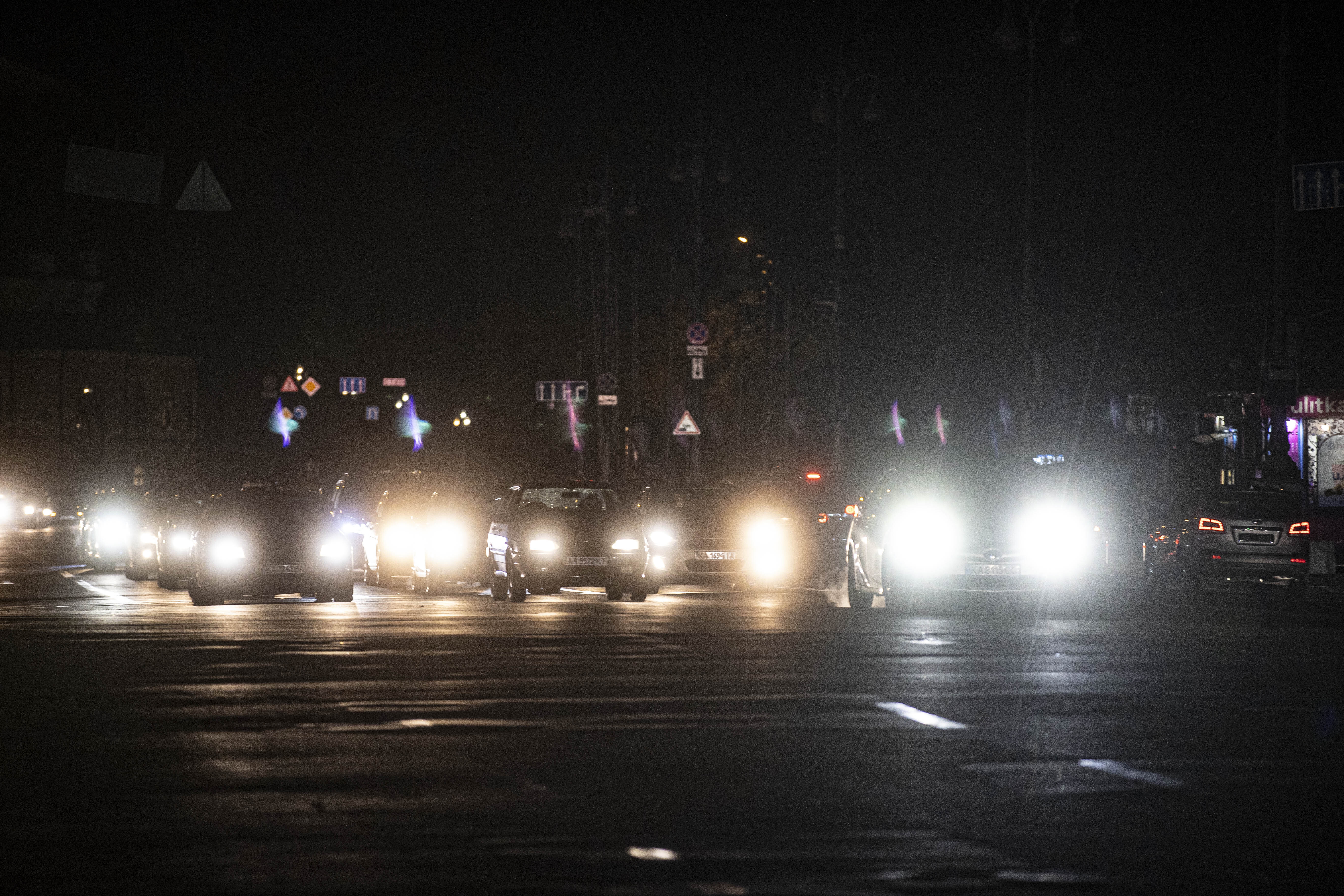 A street at night with several cars driving, their headlights creating bright beams in the darkness