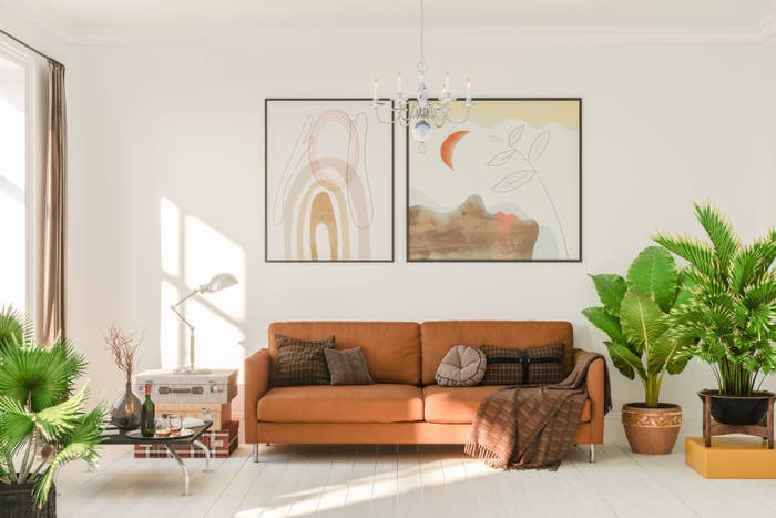Stylish living room with a brown sofa, abstract wall art, potted plants, and natural light streaming in through large windows