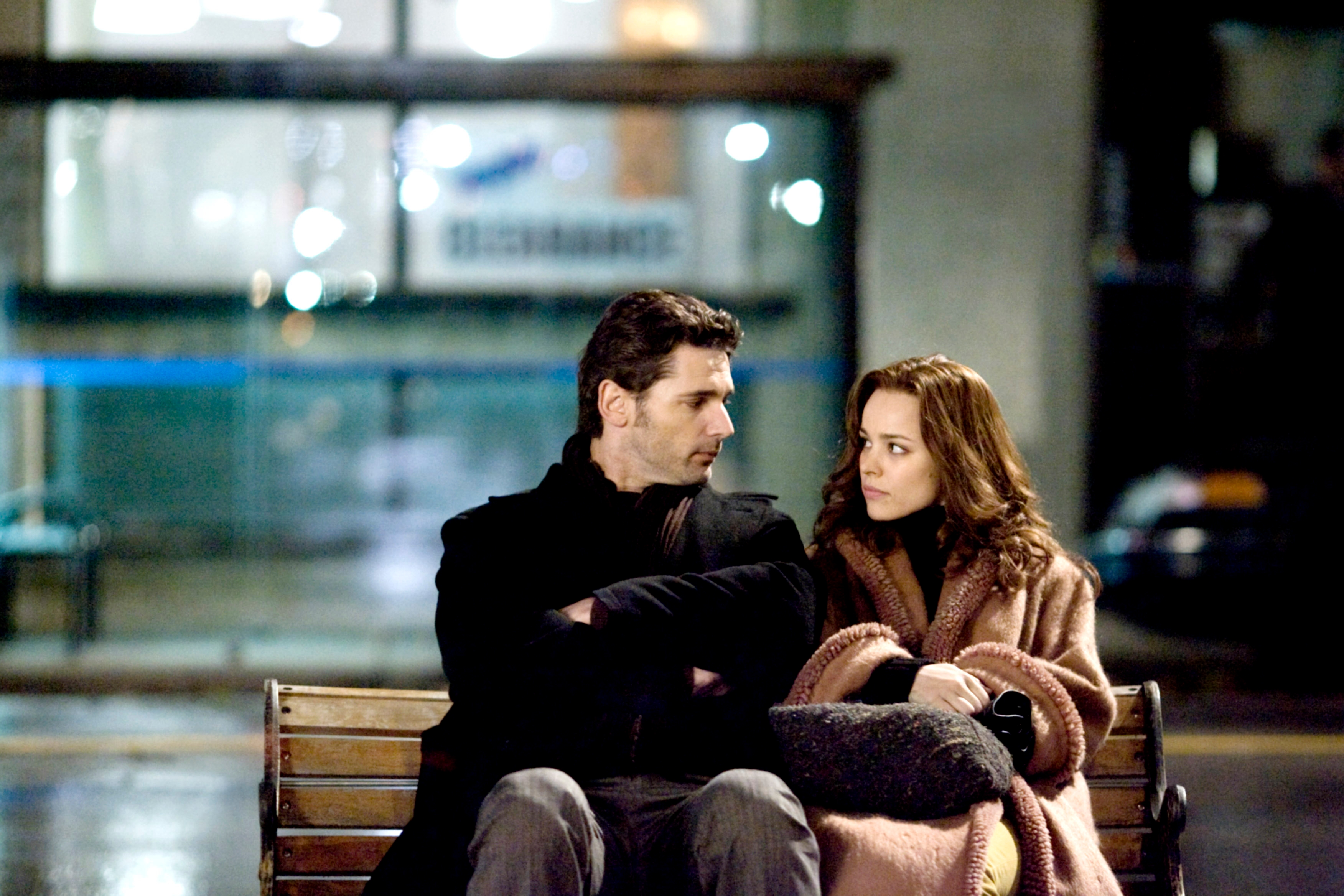 Two people sit on a bench, looking at each other. It appears to be a contemplative scene, possibly from a movie