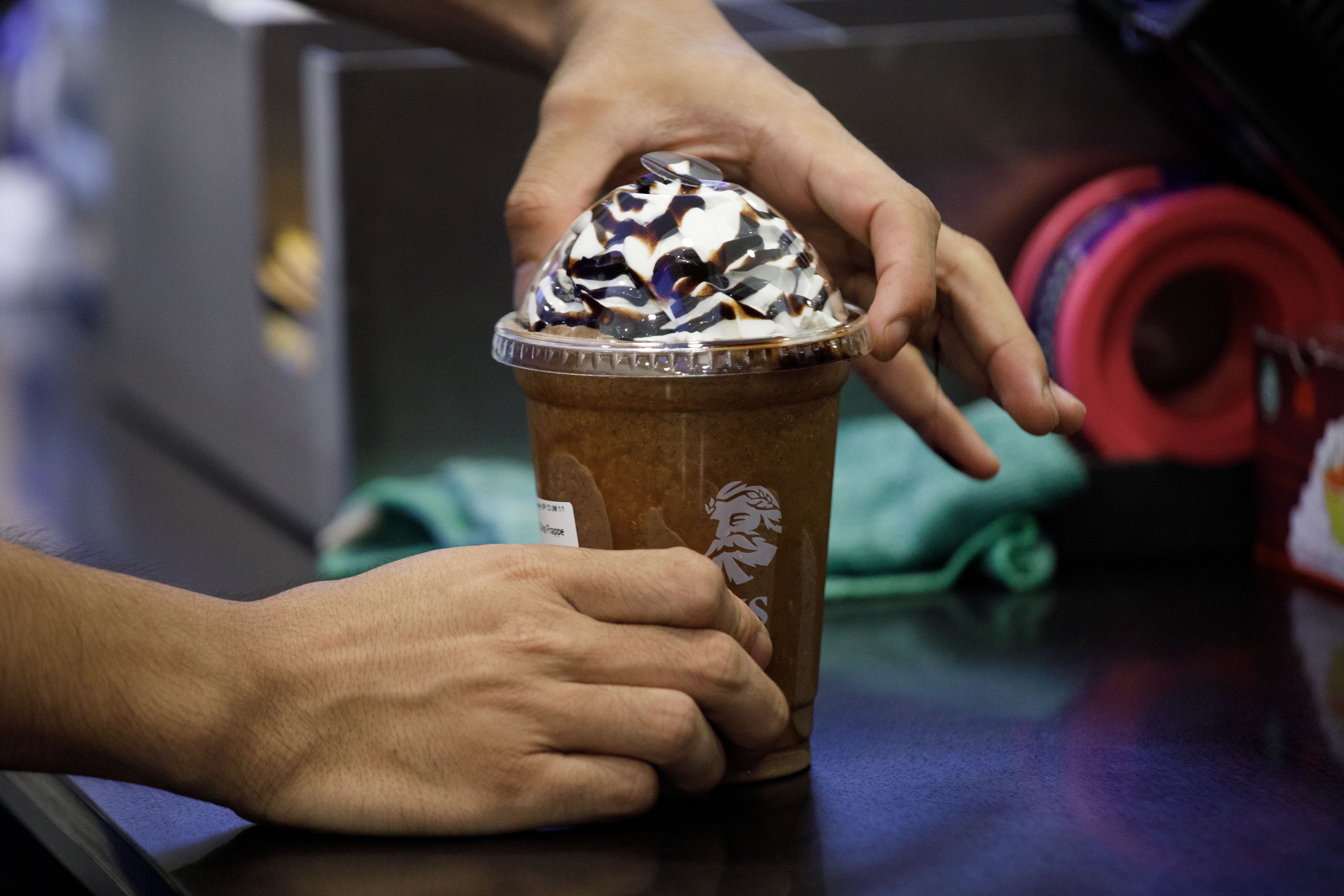 Hands holding a chocolate frappuccino topped with whipped cream and chocolate drizzle at a counter