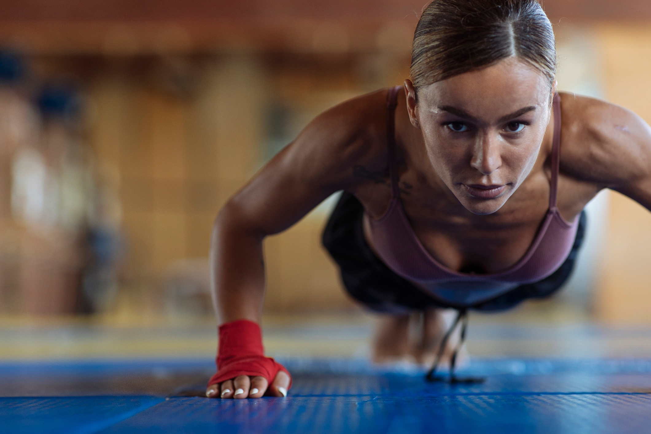 En kvinne fokusert på å gjøre push-ups, iført treningsantrekk med et håndledd, på en treningsmatte i et treningsstudio
