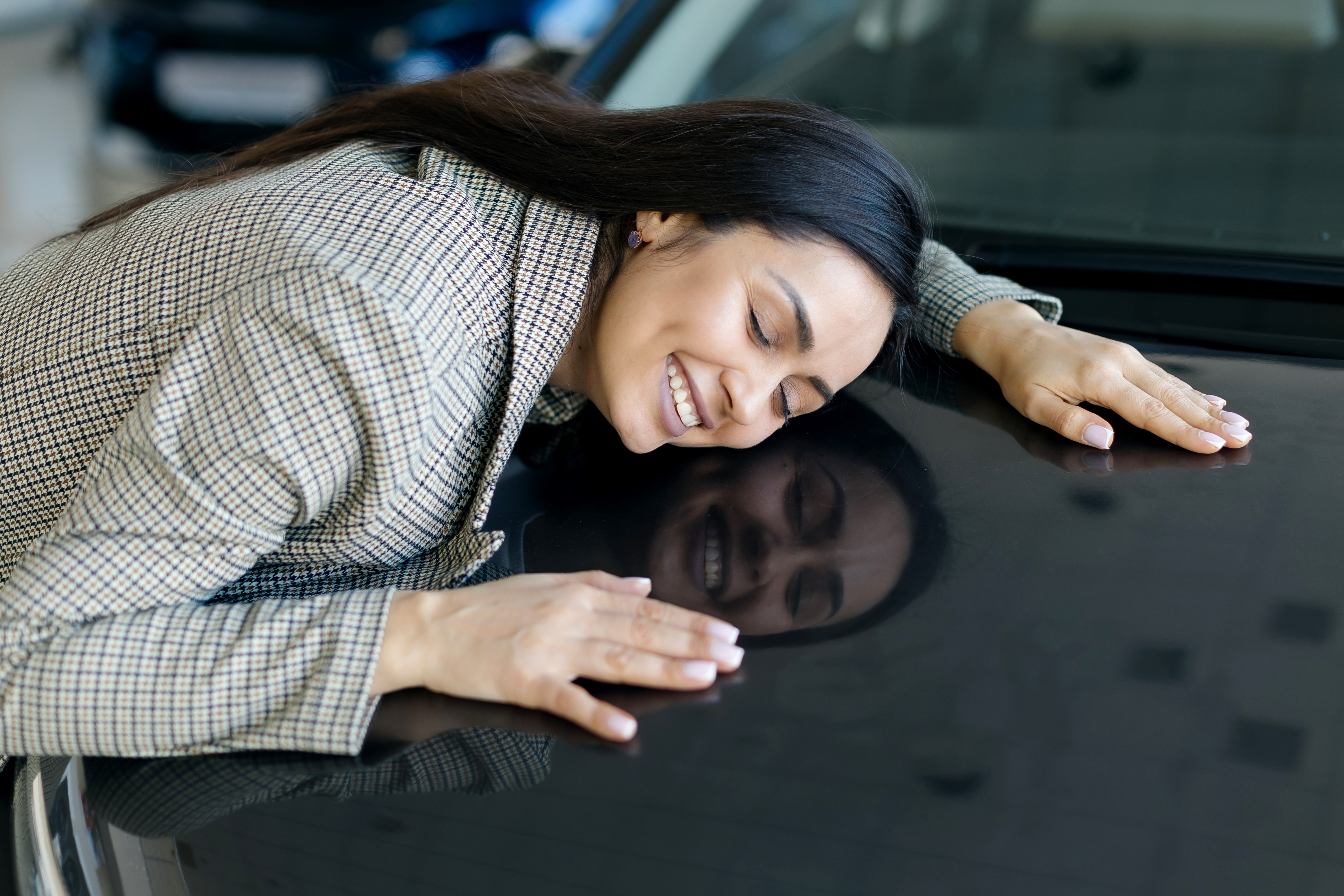 Woman joyfully hugs the hood of a car, eyes closed and smiling, reflecting a sense of satisfaction and appreciation