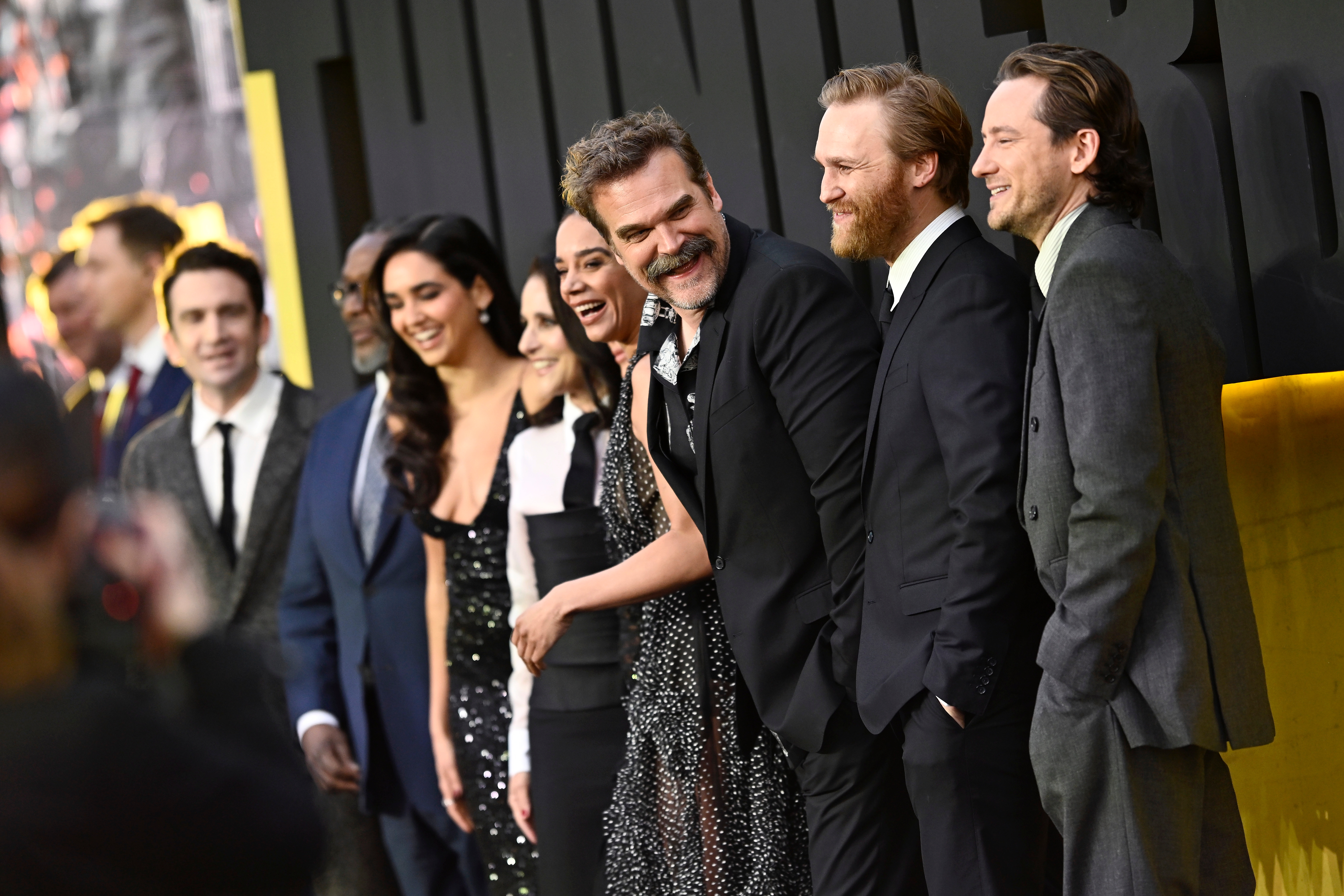 Group of celebrities in formal attire smiling on the red carpet at a premiere event