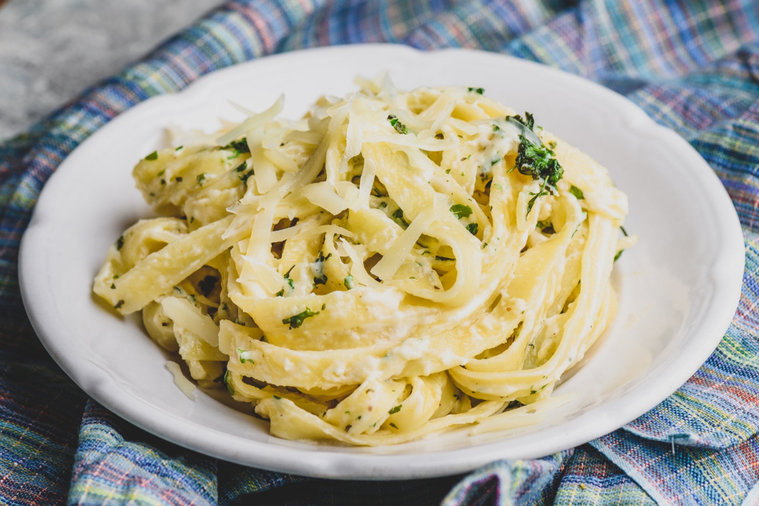 A plate of creamy pasta topped with grated cheese and herbs, set on a cloth