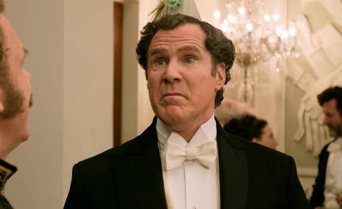 Two people talking at a formal party. One wears a tuxedo with a white bow tie and has a party hat. People are mingling in the background