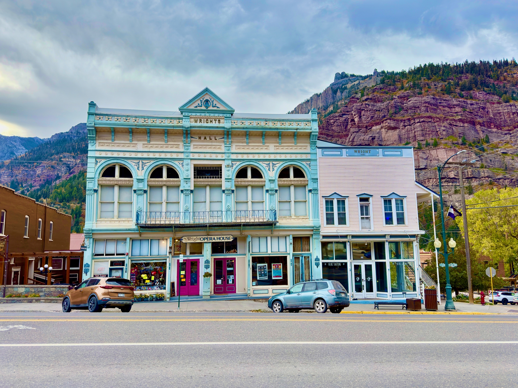 Historic buildings with arched windows on a street, set against a mountainous backdrop. Cars are parked in front