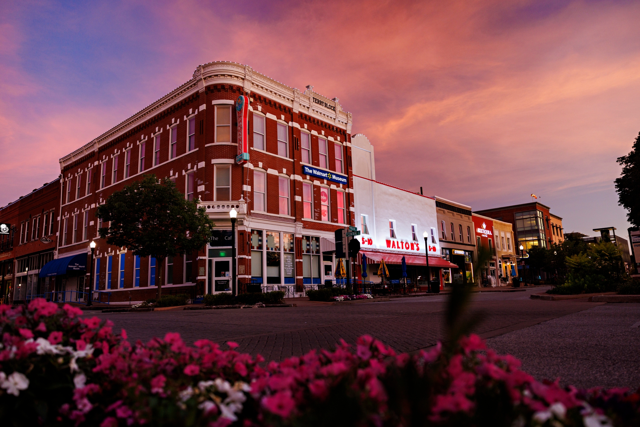 Historic brick building with Walton's sign under a twilight sky, surrounded by blooming flowers