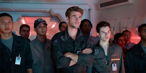 A group of people in military-style outfits gather in a high-tech room, focused intently, possibly in a scene from a movie or show