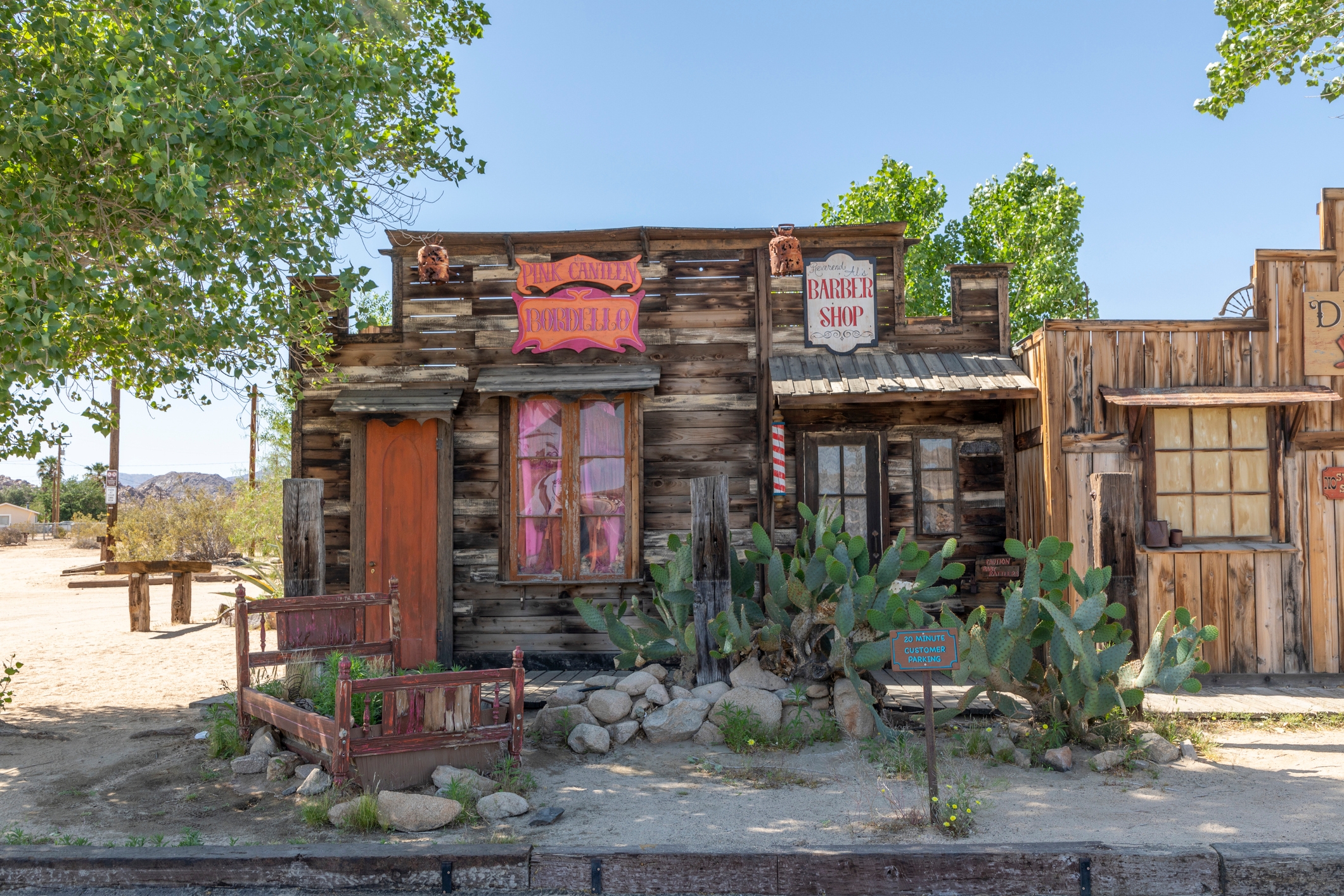 Old Western-style barbershop facade with weathered wood, a porch, and desert plants in the foreground under a clear sky