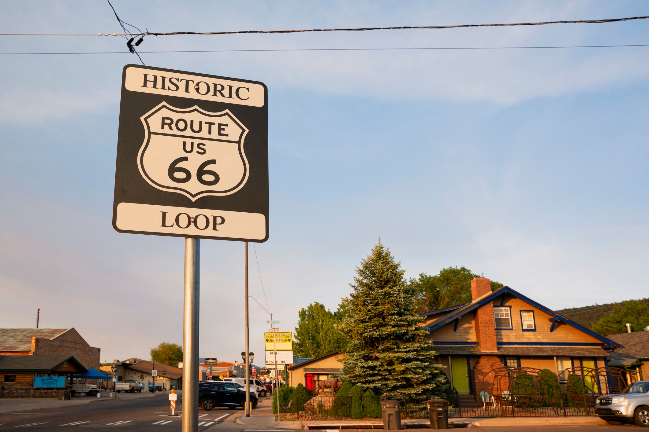 Route 66 road sign in a small town with a few buildings and trees in the background