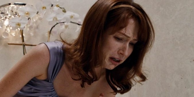 A woman in distress, in a formal gown, clutches her stomach. Orchids are in the background