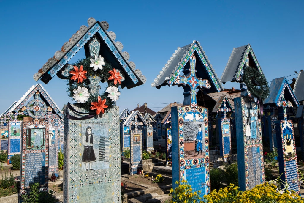 Ornately decorated tombstones with colorful carvings and floral wreaths in a vibrant cemetery, under a clear sky