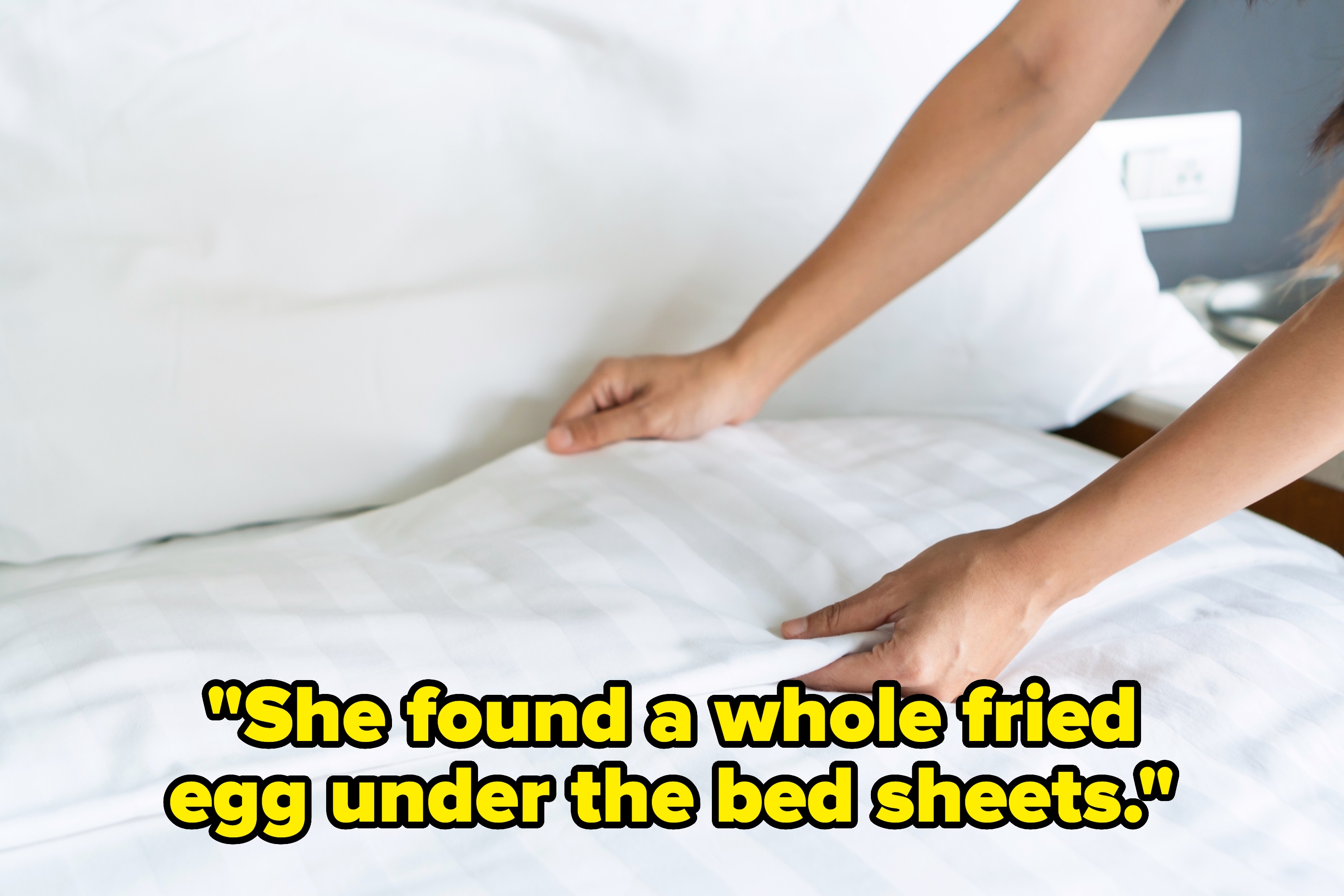 Person neatly making a bed, smoothing out a white sheet