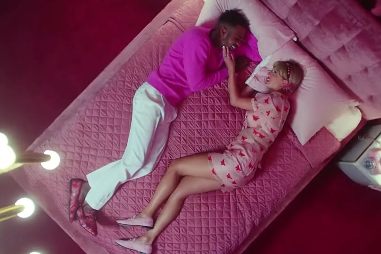 Taylor Swift and someone else lie on a bed, facing each other in the Lover music video