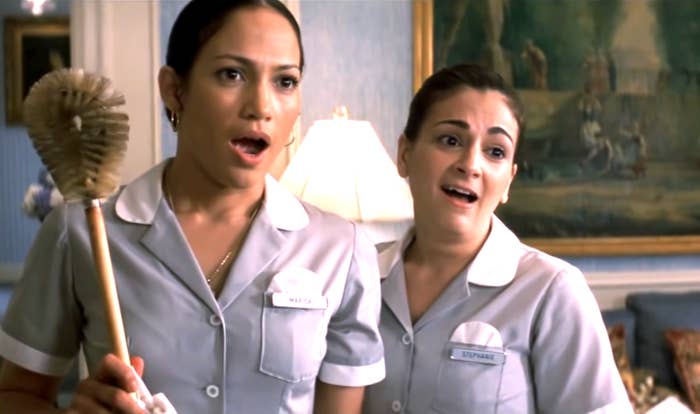 Two women in maid uniforms stand inside a room, looking surprised. One holds a cleaning brush. A painting and lamp are visible in the background
