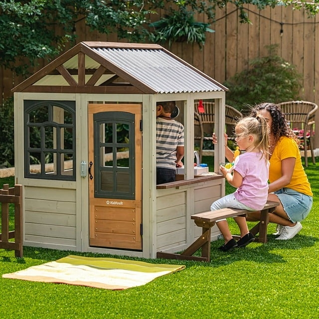 Child and adult play outside a wooden playhouse with a bench, suggesting it's an engaging outdoor activity or playhouse for kids