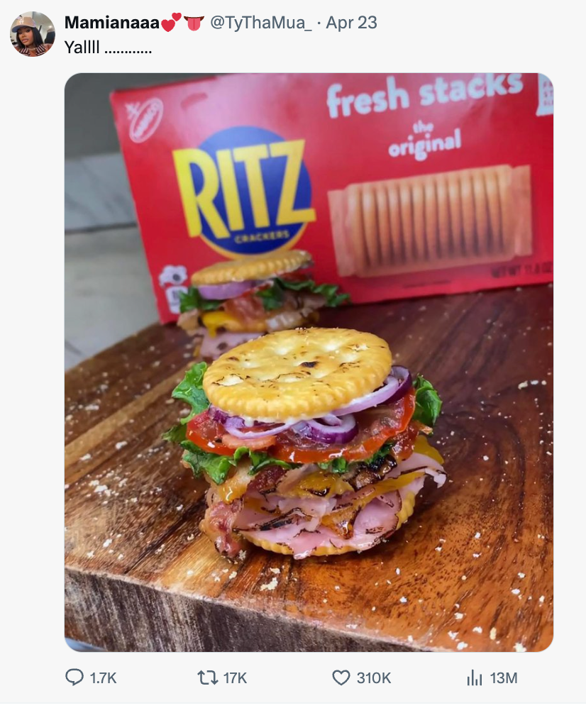 A sandwich made with Ritz crackers, lettuce, bacon, red onions, and sauces is displayed on a cutting board near a Ritz crackers box