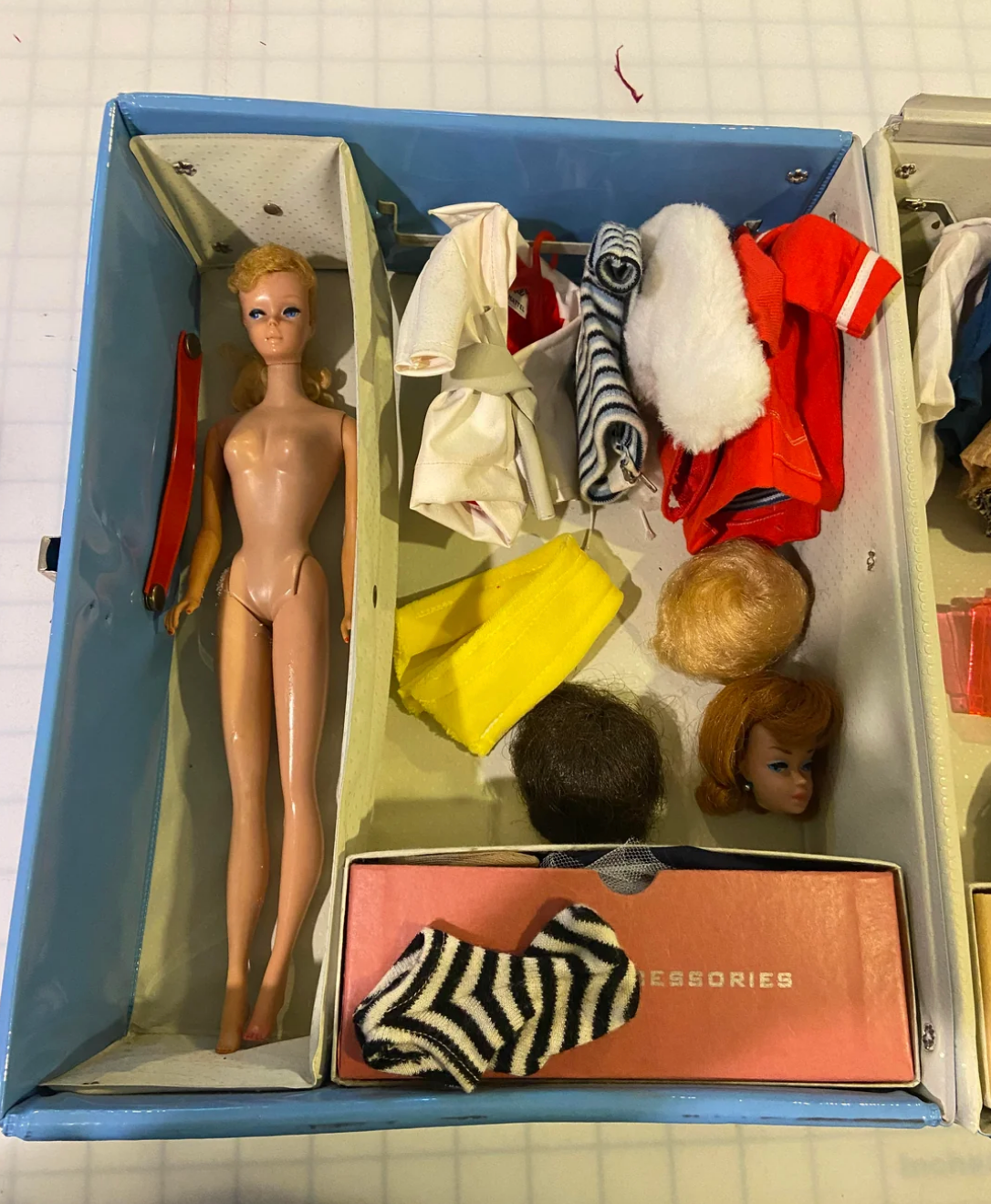 Vintage doll with detachable heads and various clothing items, including a striped bathing suit, displayed in an open box labeled "Accessories."