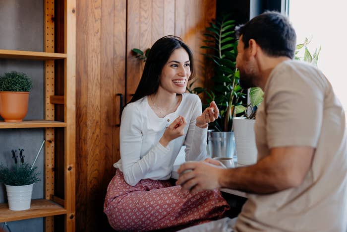 Woman in casual clothing chatting happily with a man in a cozy, plant-filled room