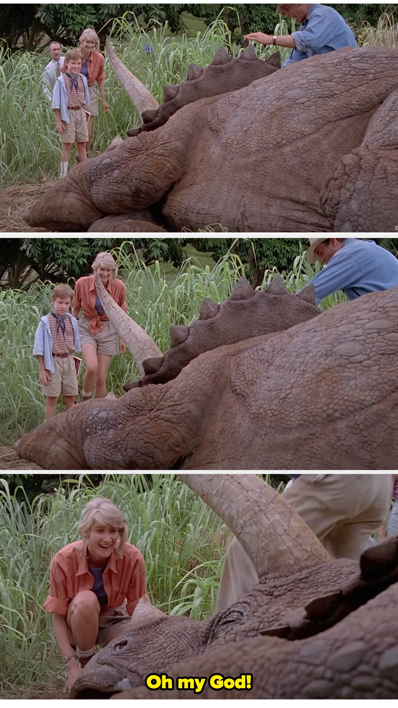 Three people examine a large triceratops lying on the ground in a jungle setting. Ellie in safari attire reacts with surprise and awe as she kneels in front of it