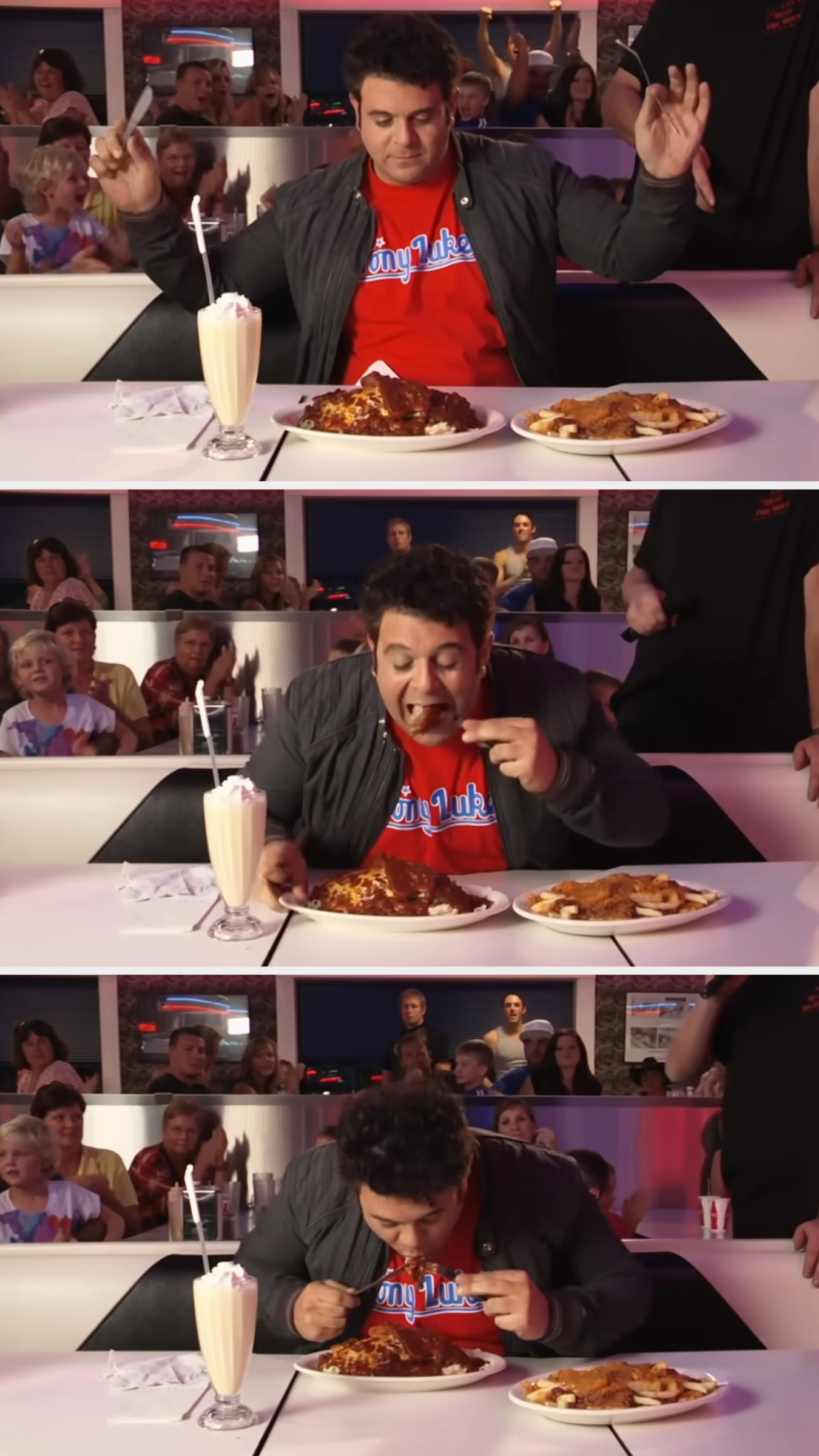 Person enthusiastically participating in a food challenge at a diner, eating large portions of food with a milkshake, while a crowd watches