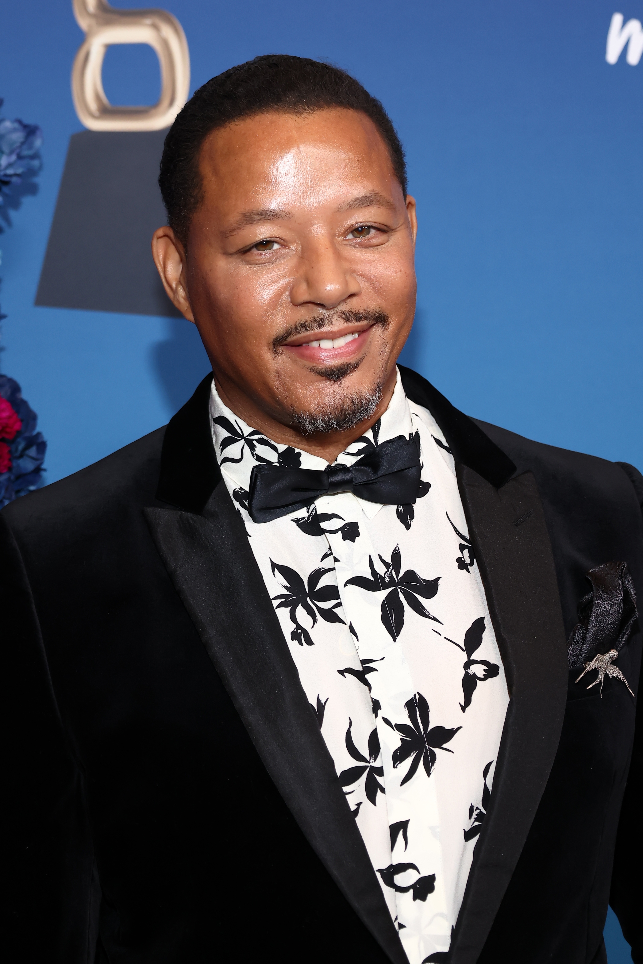 Terrence Howard in floral-patterned shirt and velvet jacket smiles on red carpet