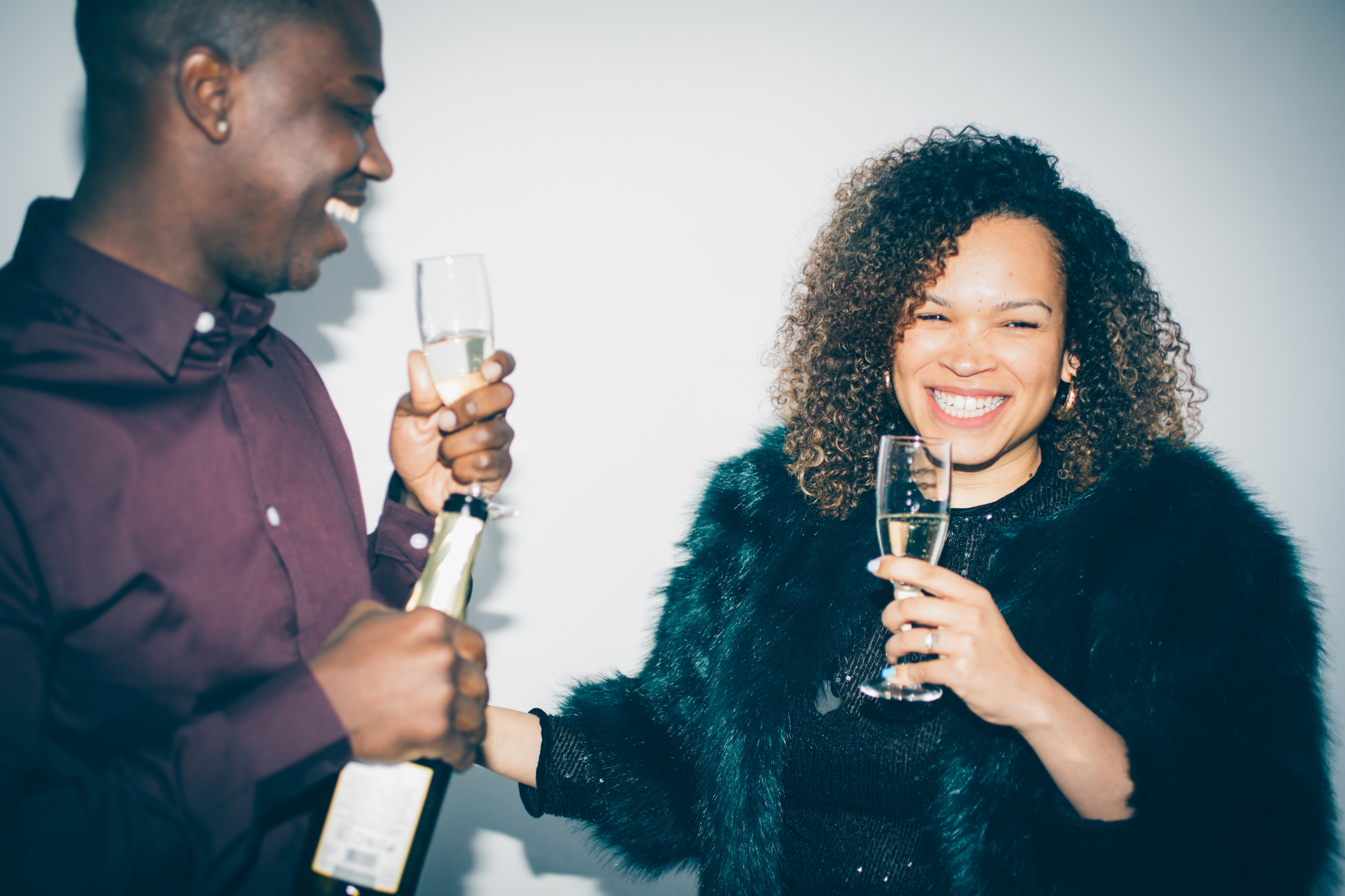 Two people smiling and toasting with champagne, dressed in elegant evening wear, suggesting a celebratory or festive atmosphere