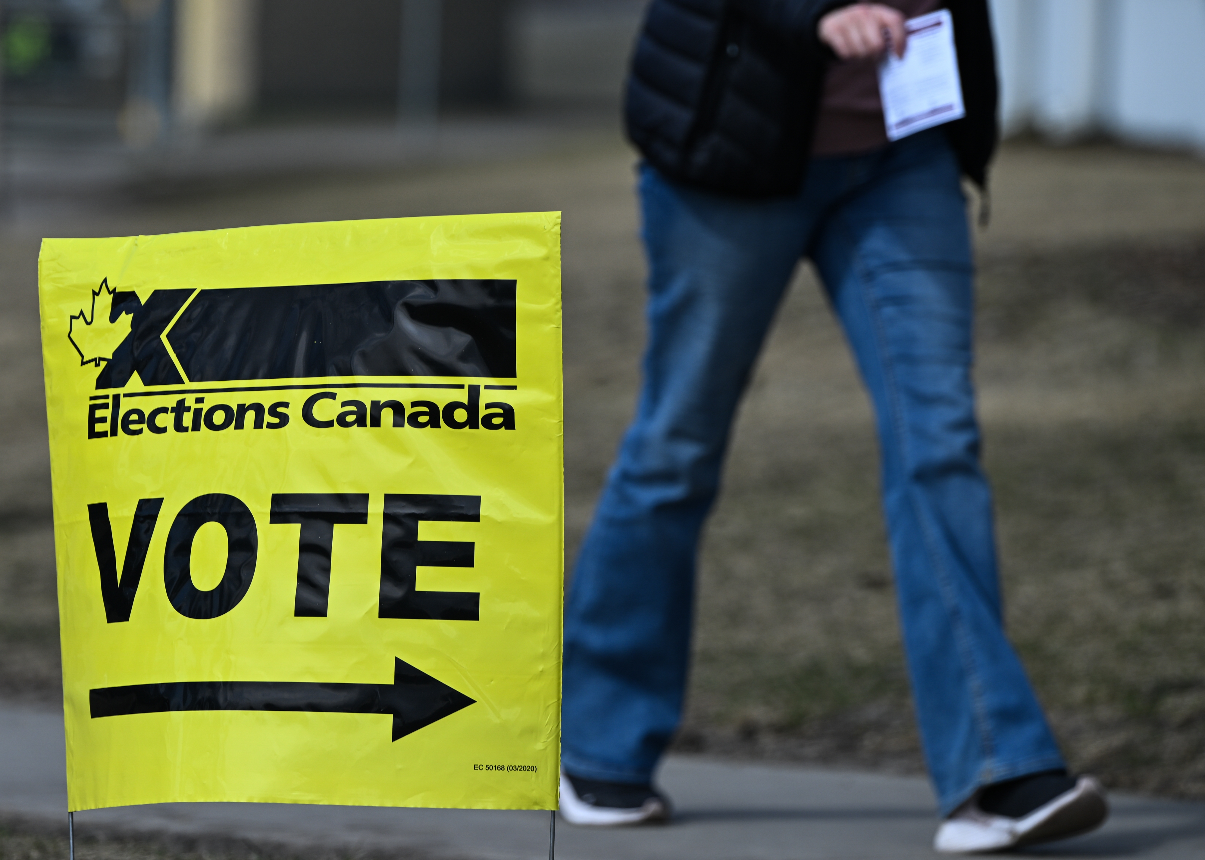 Person walking past a "Vote" sign for Elections Canada, indicating a polling station location