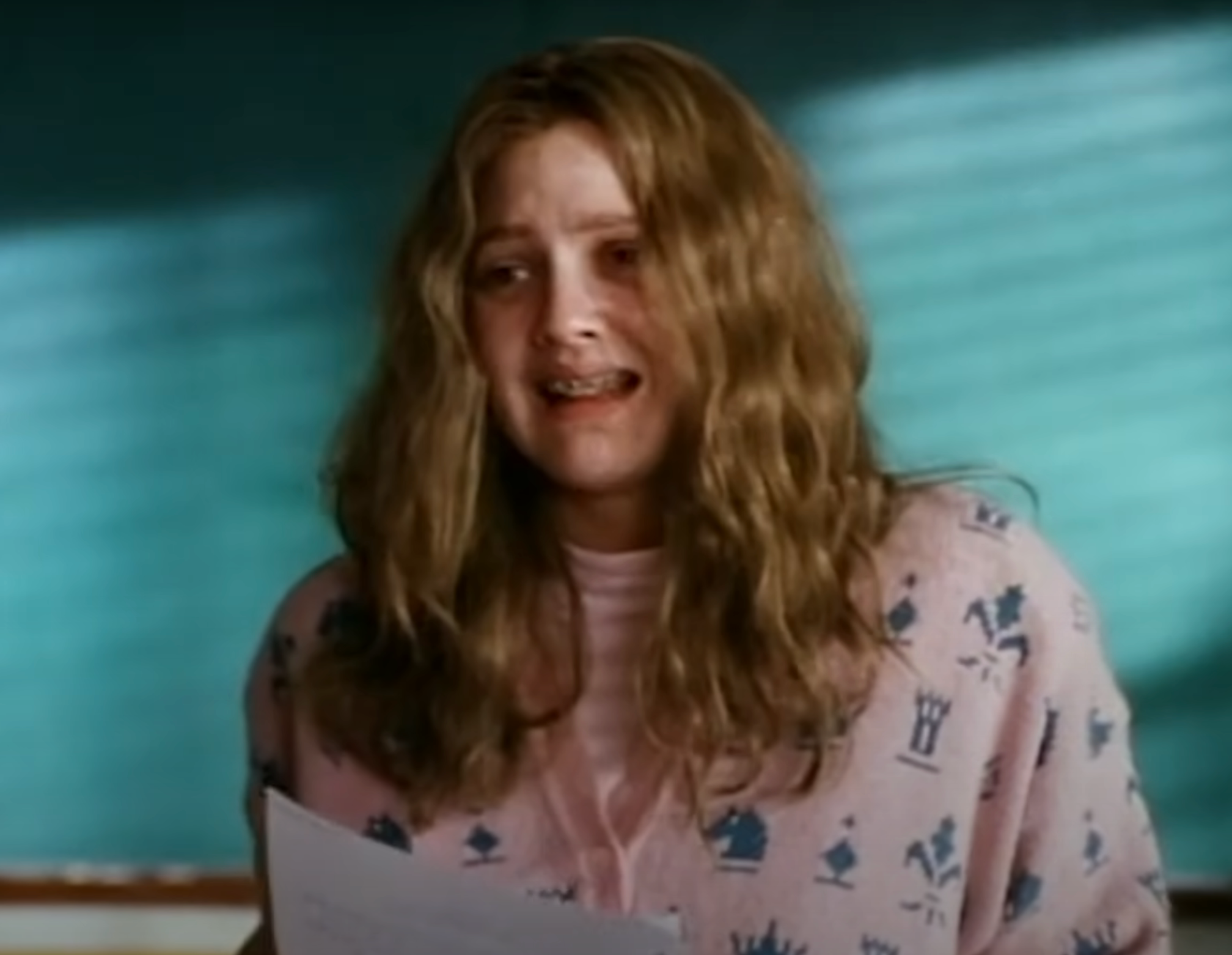 Drew with long, wavy hair and braces holds papers