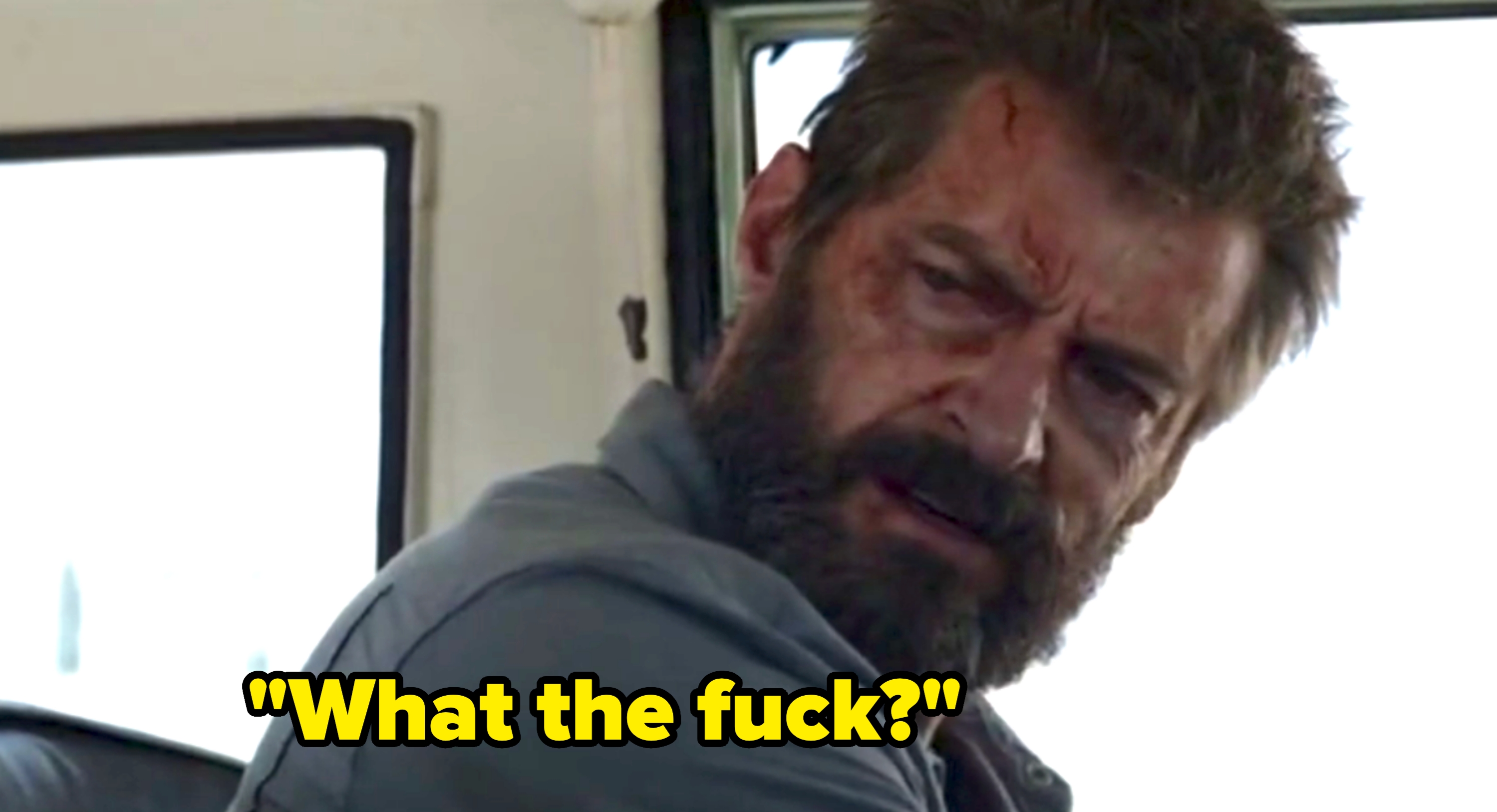 A man with a rugged appearance and a beard looks over his shoulder with concern, sitting inside a vehicle