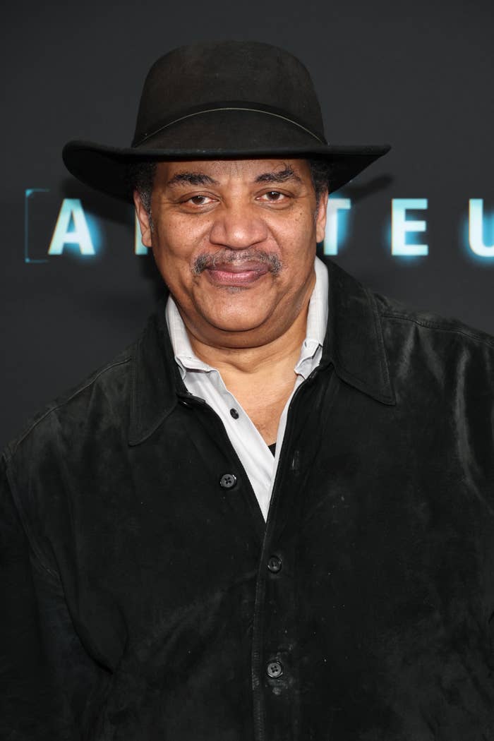 A person wearing a black hat and jacket over a light shirt at a media event