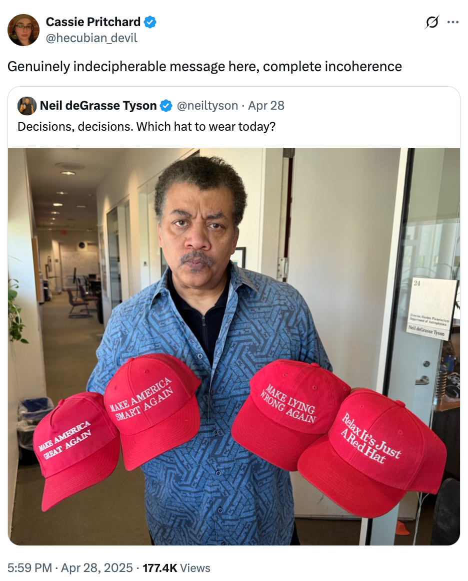 Neil deGrasse Tyson holds three red hats with different humorous slogans, expressing indecision on which to wear