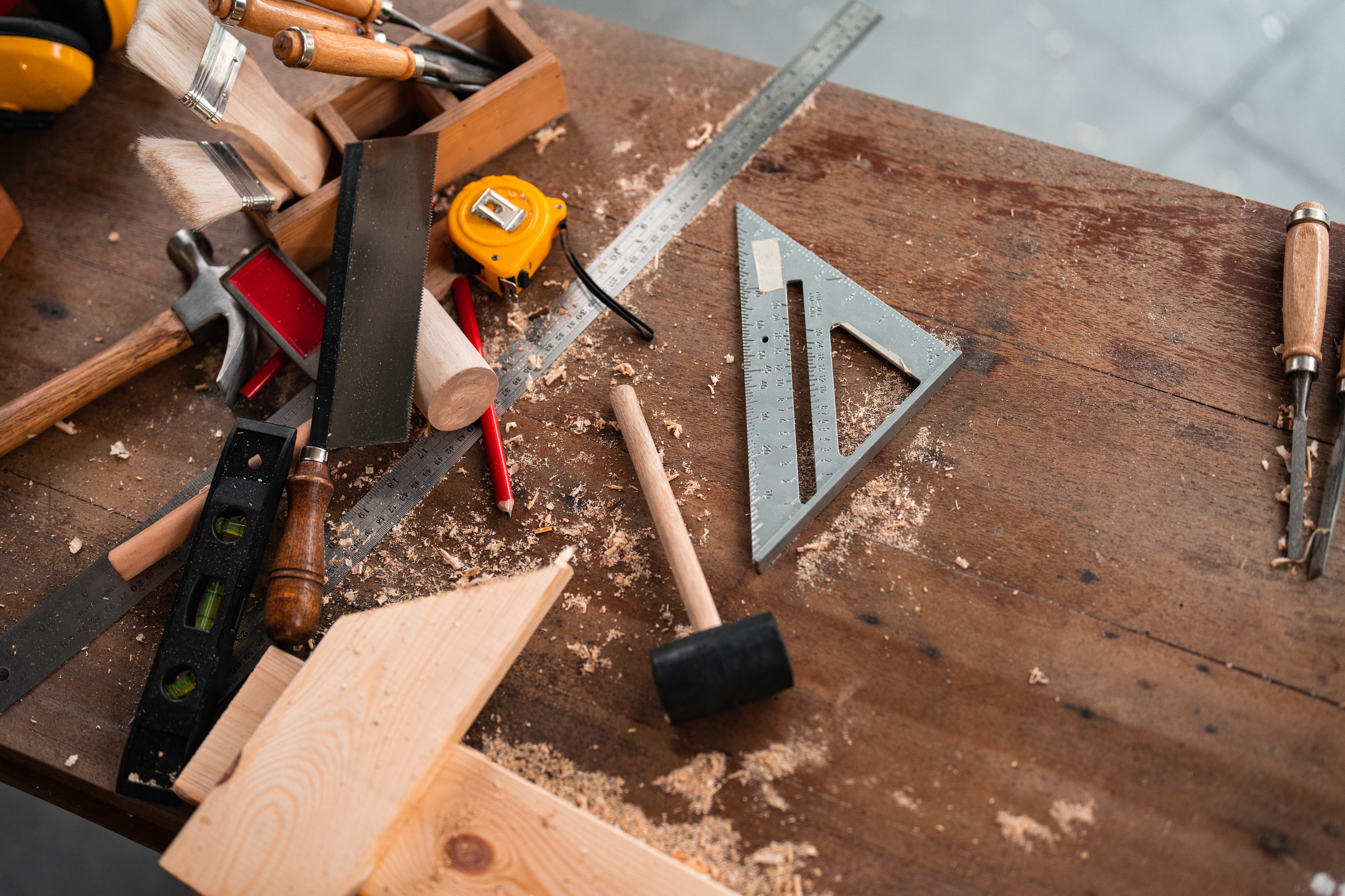 Woodworking tools on a workbench, featuring a hammer, square, tape measure, and chisels, surrounded by wood shavings and blocks
