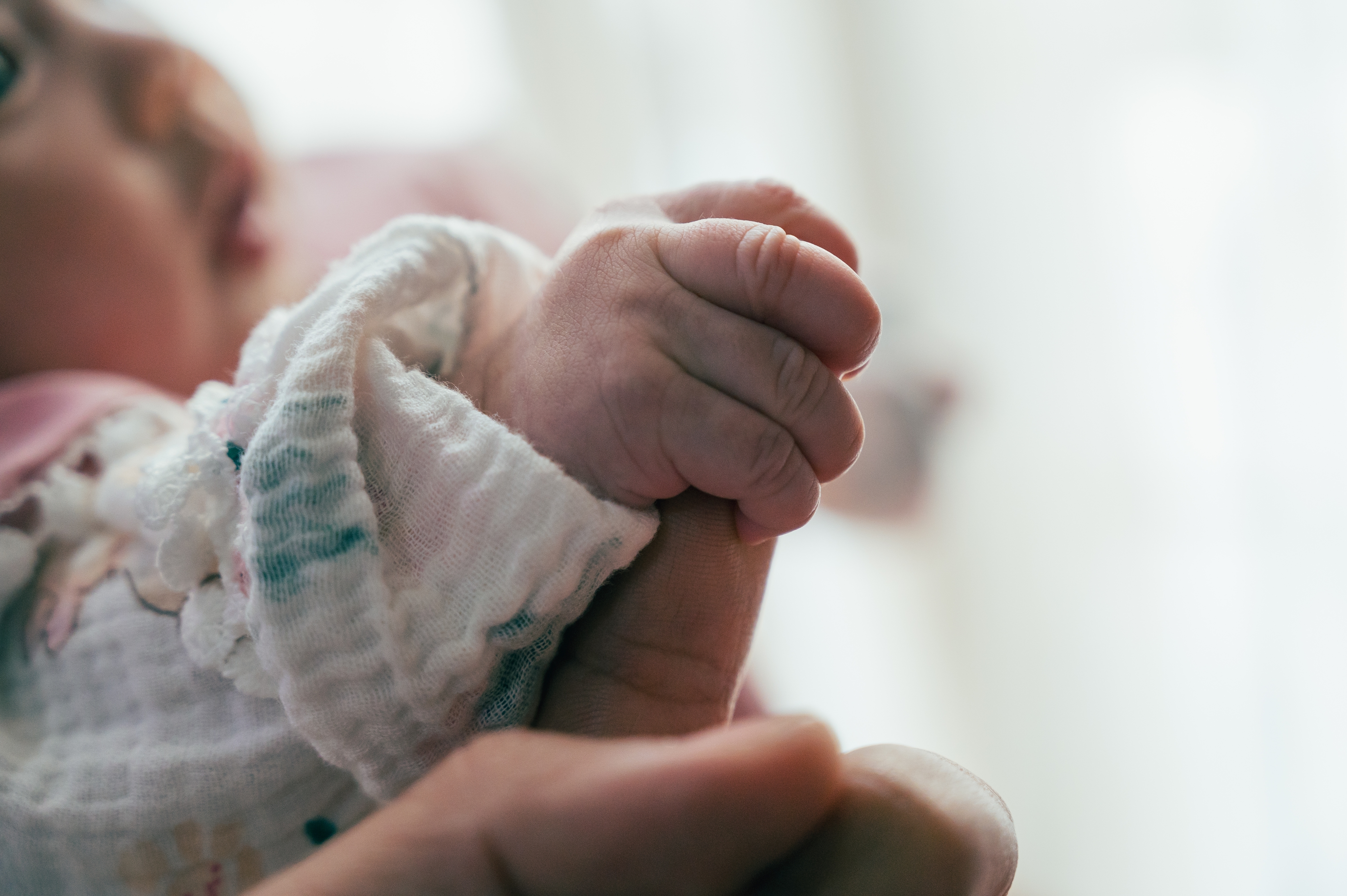 Close-up of a baby gently gripping an adult's finger, symbolizing connection and love