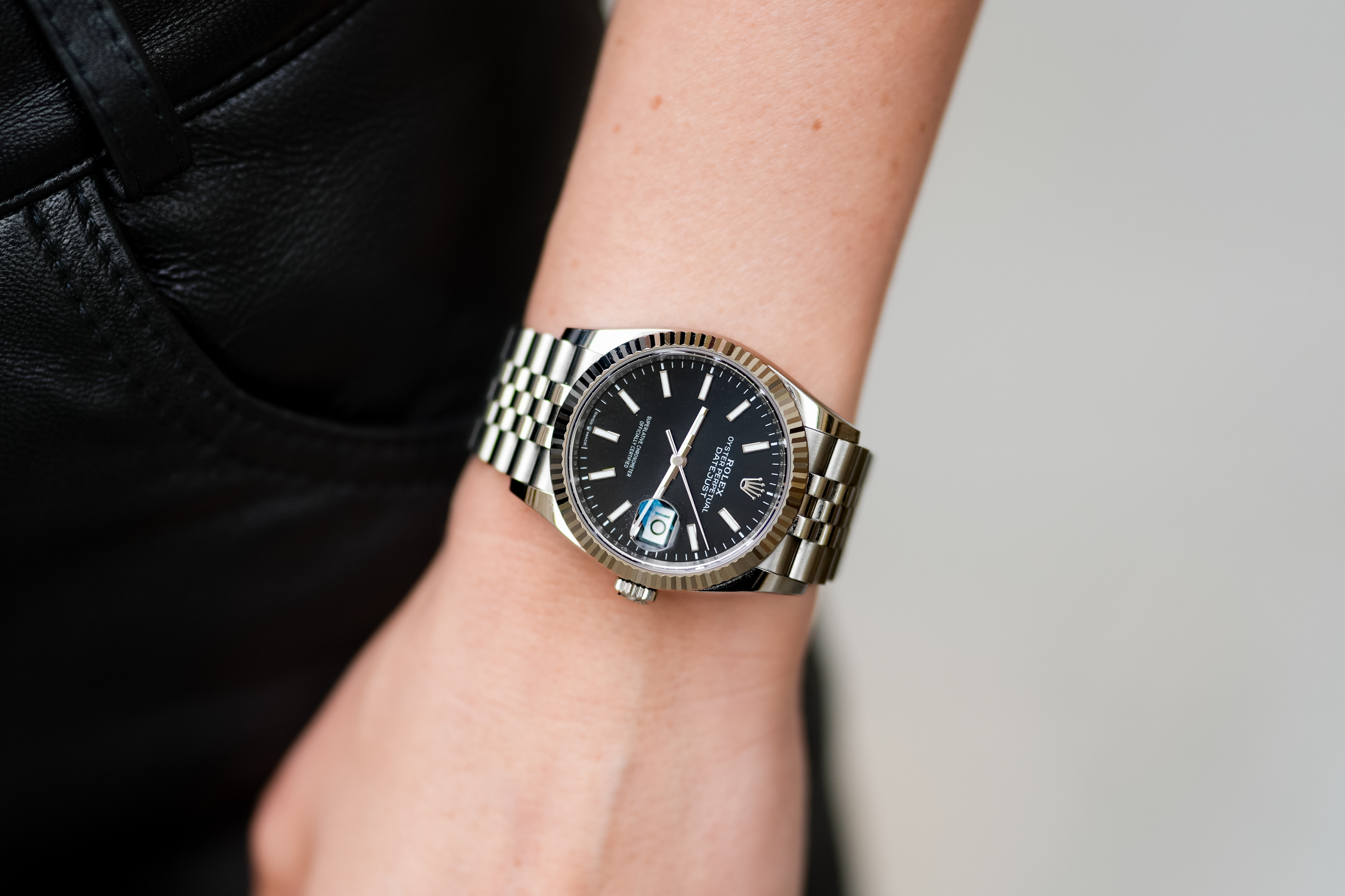 Close-up of a wrist wearing a luxury watch with a silver bracelet and black dial. Date feature visible, symbolizing success and style in work settings